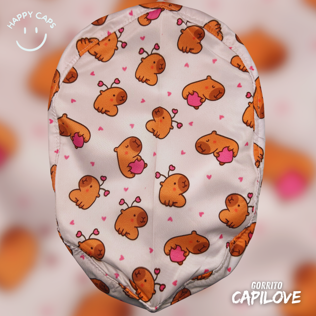 Surgical cap with cartoon capybara pattern, small pink hearts, and text Happy Caps and Gorrito Capilove on a blurred background.