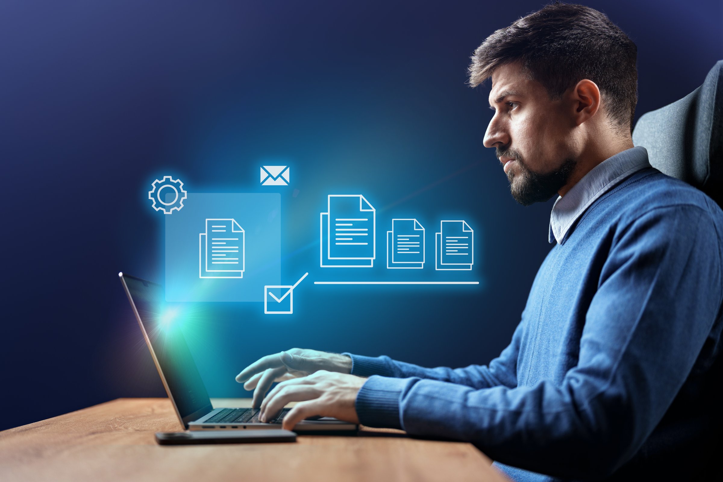 A young man sits at a wooden desk in a contemporary office, focusing on his laptop. Digital icons representing emails and documents appear around him, highlighting productivity.