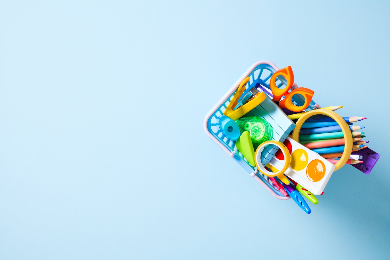 Back to School Concept: A shopping basket filled with colorful school and art supplies on a light blue background with copy space.