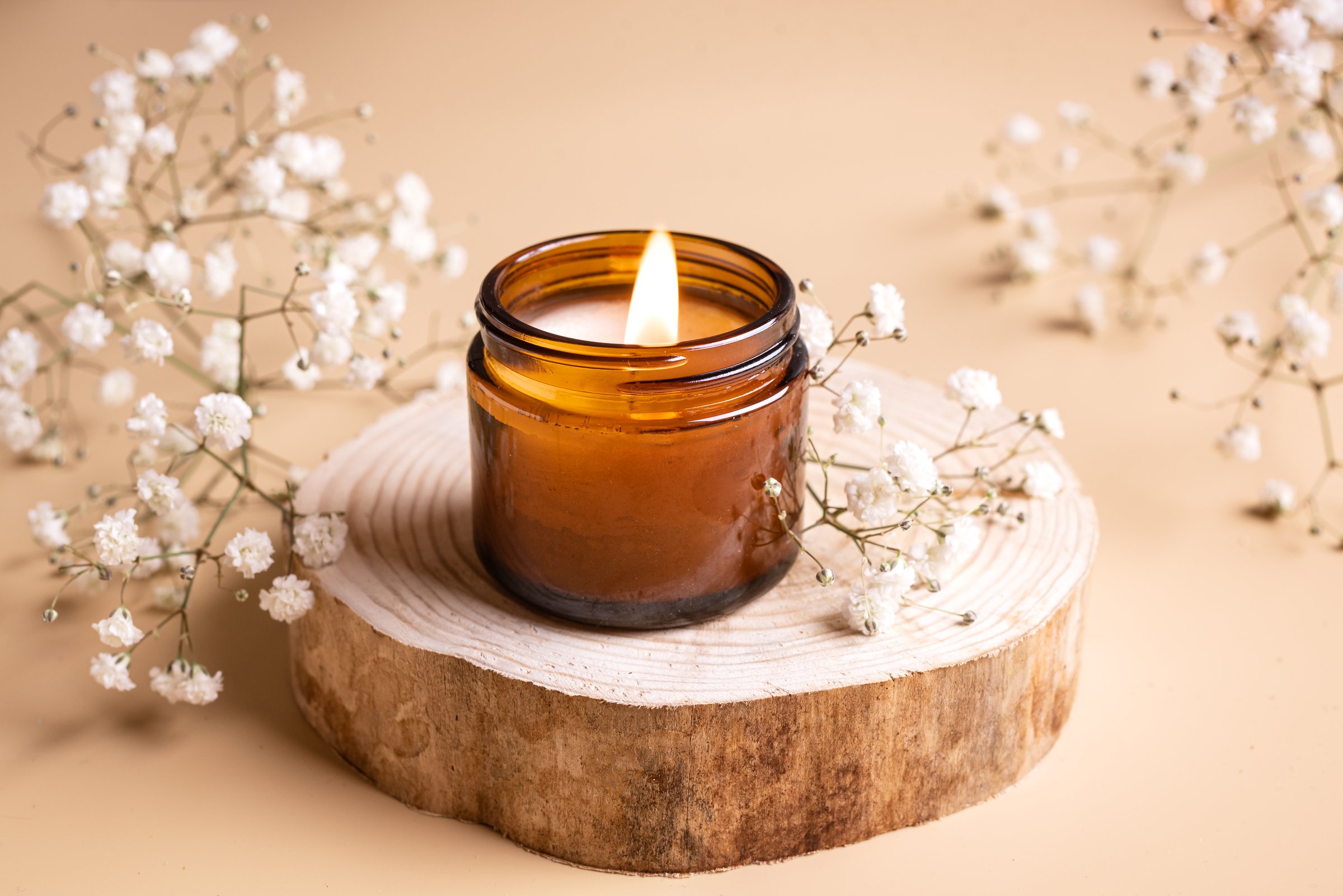 Burning soy wax aroma candle and white gypsophila flowers close up. Scented massage candle, relaxation and home interior decor concept.
