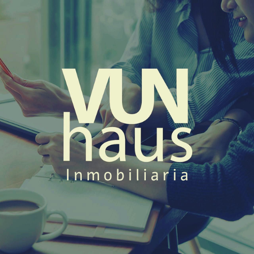 Two people reviewing documents at a table with coffee, overlay text reads VUN haus Inmobiliaria.