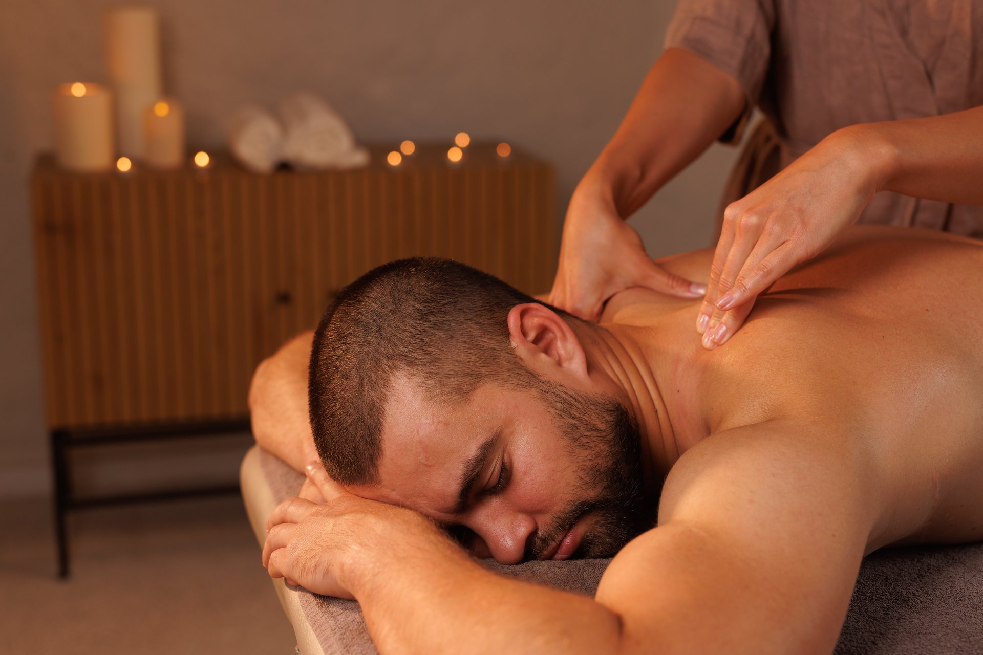 Relaxing neck massage, healthy massaging rehab concept. Close-up hands of woman masseur doing wellness medical relaxing massage for male patient in dark medical office in shadow. Copy ad text space