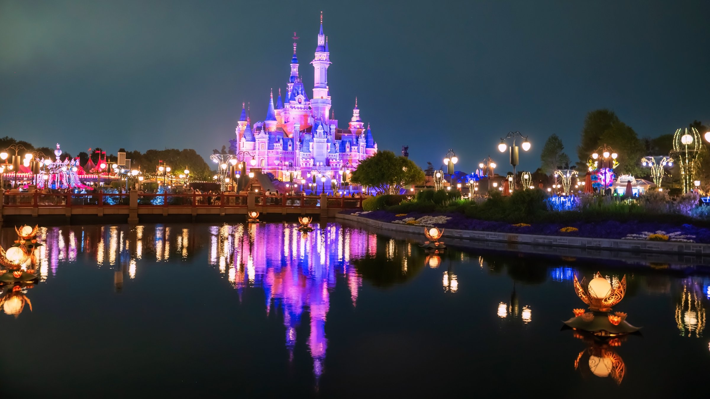 Shanghai, China - April 11, 2025: Disney Castle light up at night with skyline reflection on pond. The most famous theme park in China.