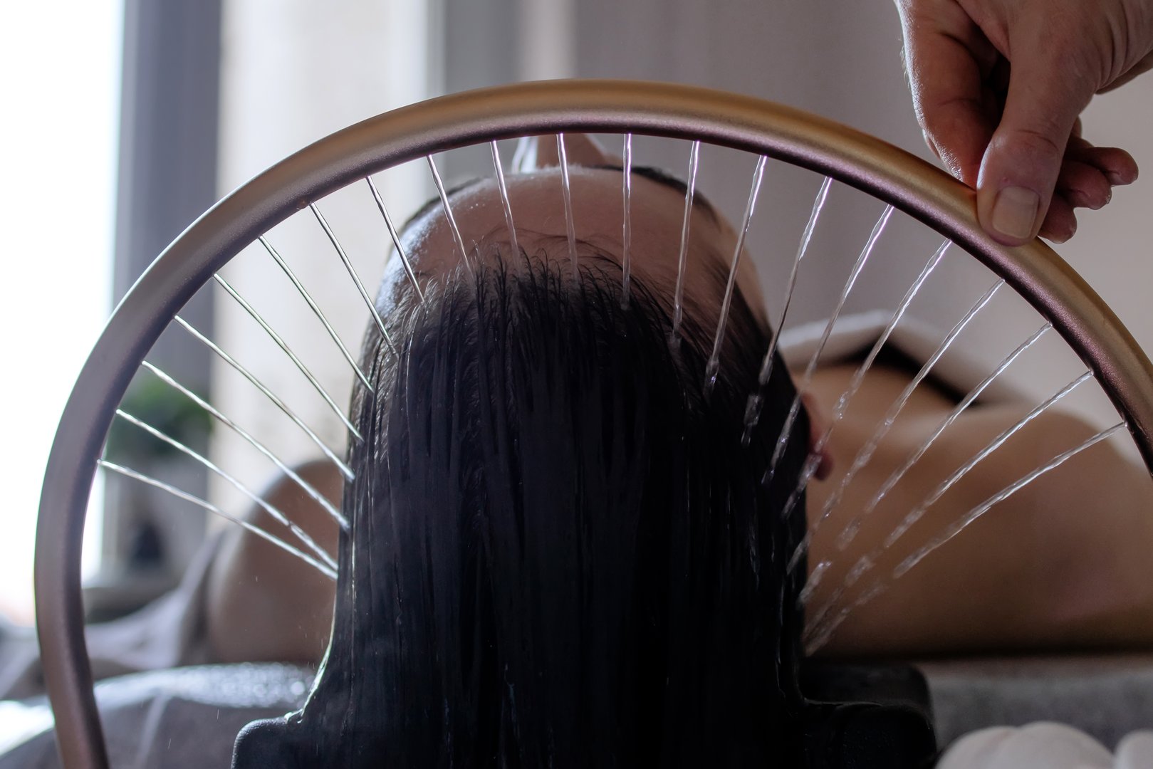 Close-up of a woman receiving a head massage during a Japanese head spa treatment with water flowing from a special hair washing tool, focusing on the scalp relaxation and beauty therapy