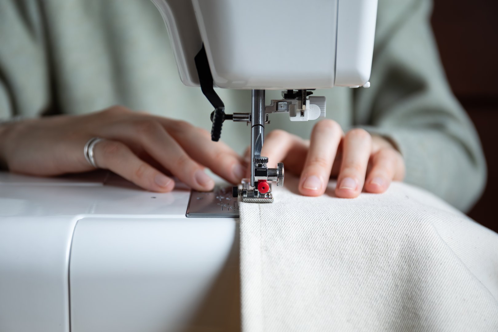 a front view of a woman's hands wearing rings, sewing beige fabric on a sewing machine