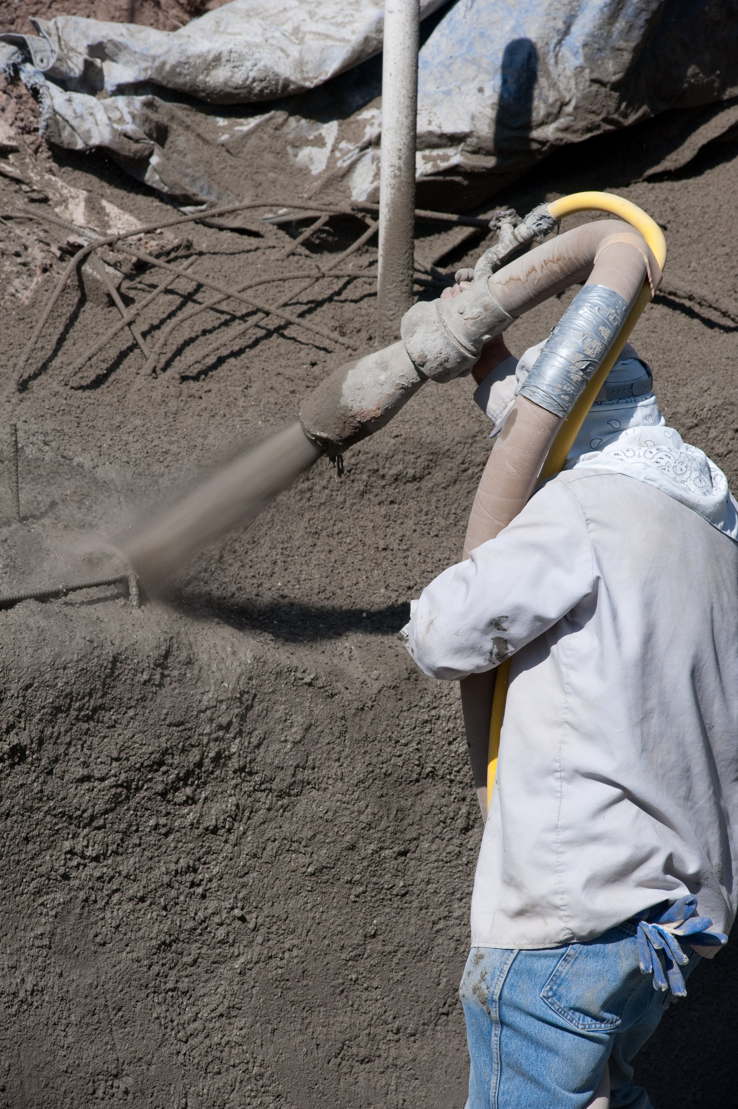Worker wearing protective clothing spraying concrete onto a surface with a hose on a construction site.
