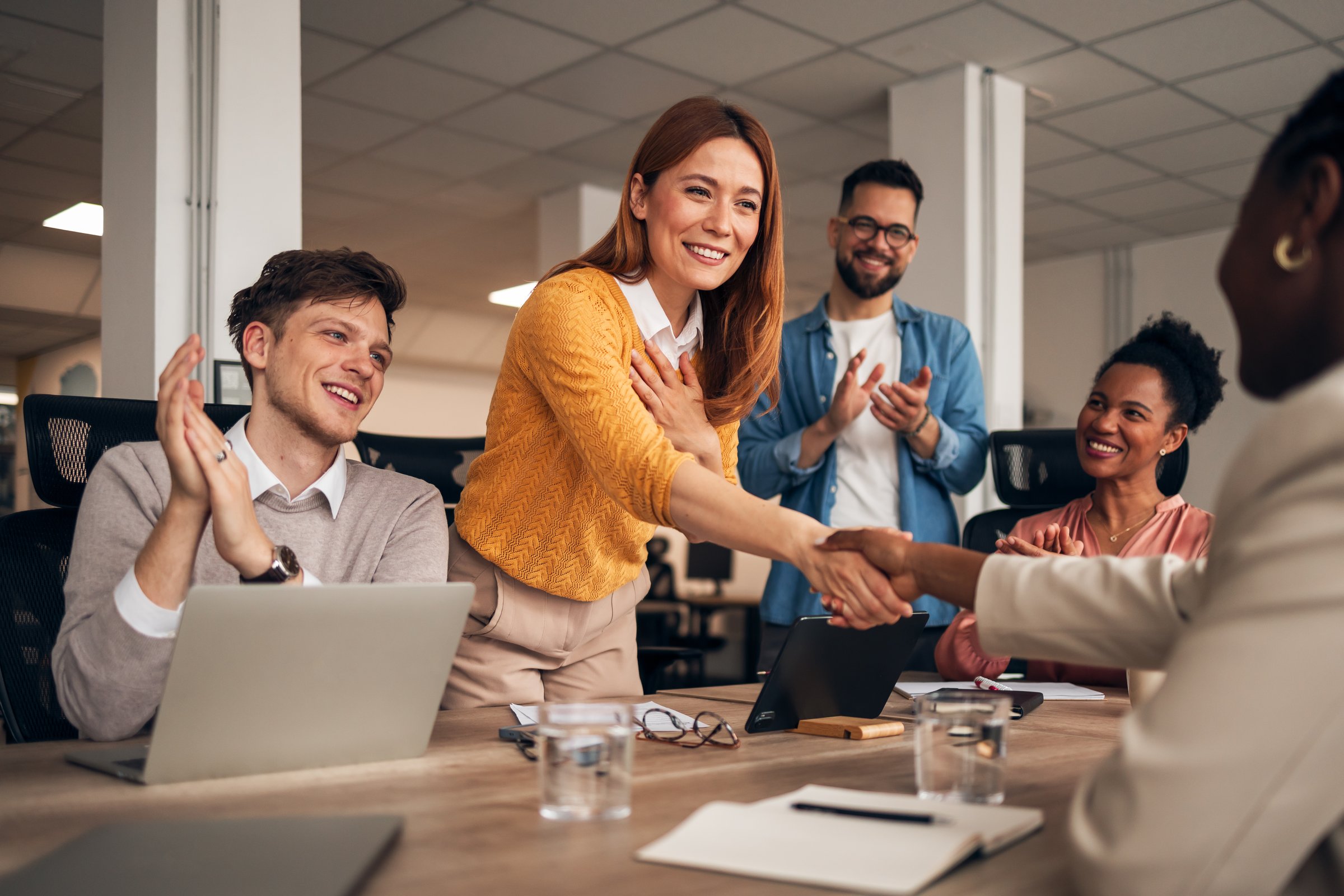 A group of smiling coworkers celebrate a positive business agreement during a meeting in the office.