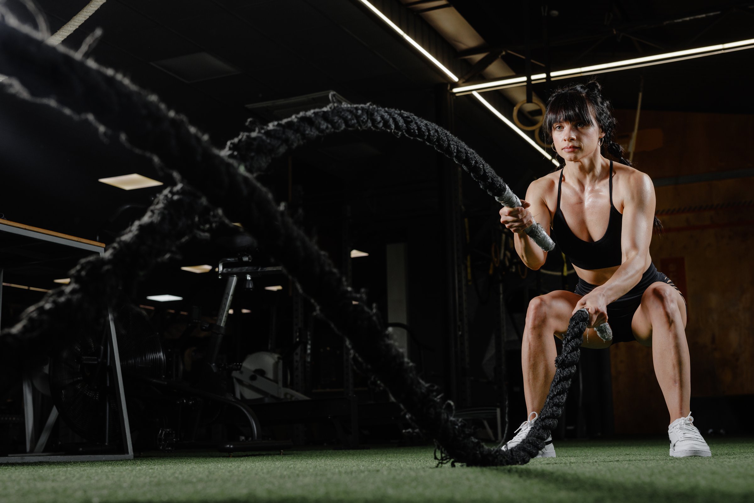 Athletic woman trains with battle ropes in gym strength workout dynamic fitness motivation and healthy lifestyle concept