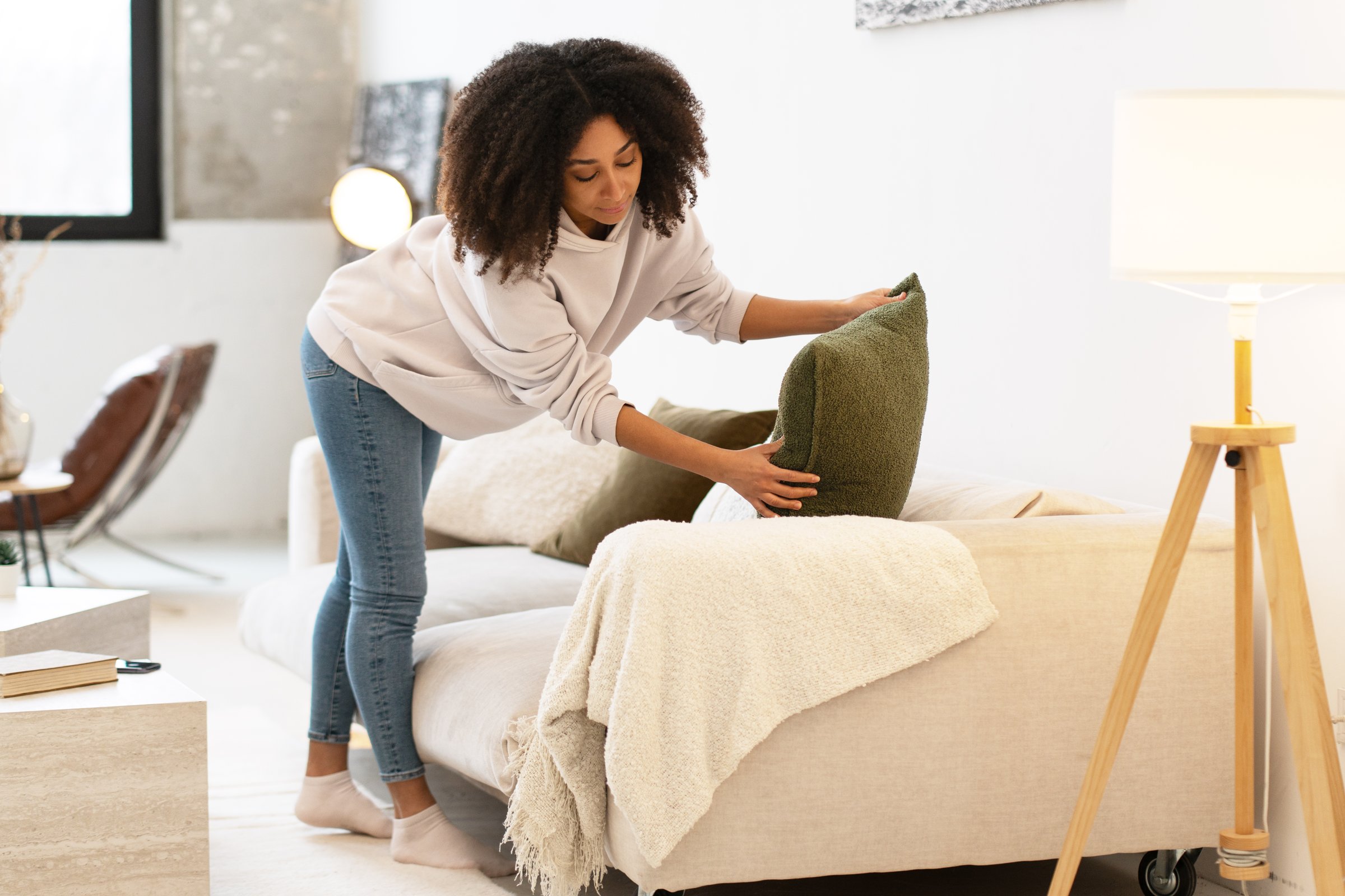 Woman tidying up her modern living room, arranging cushions on a comfortable sofa, creating a cozy and inviting atmosphere