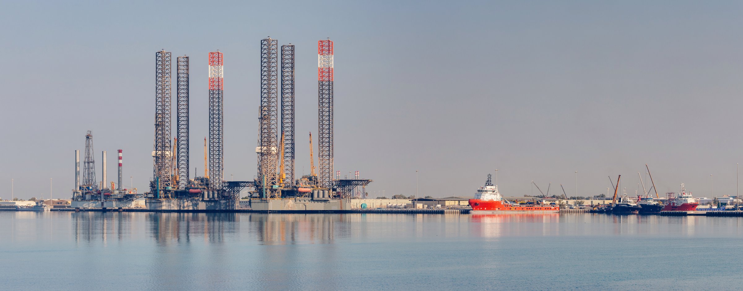 15 January 2025, Abu Dhabi, UAE: Jackup oil rig and platform supply vessel staying in harbor in calm water with cloudy sky