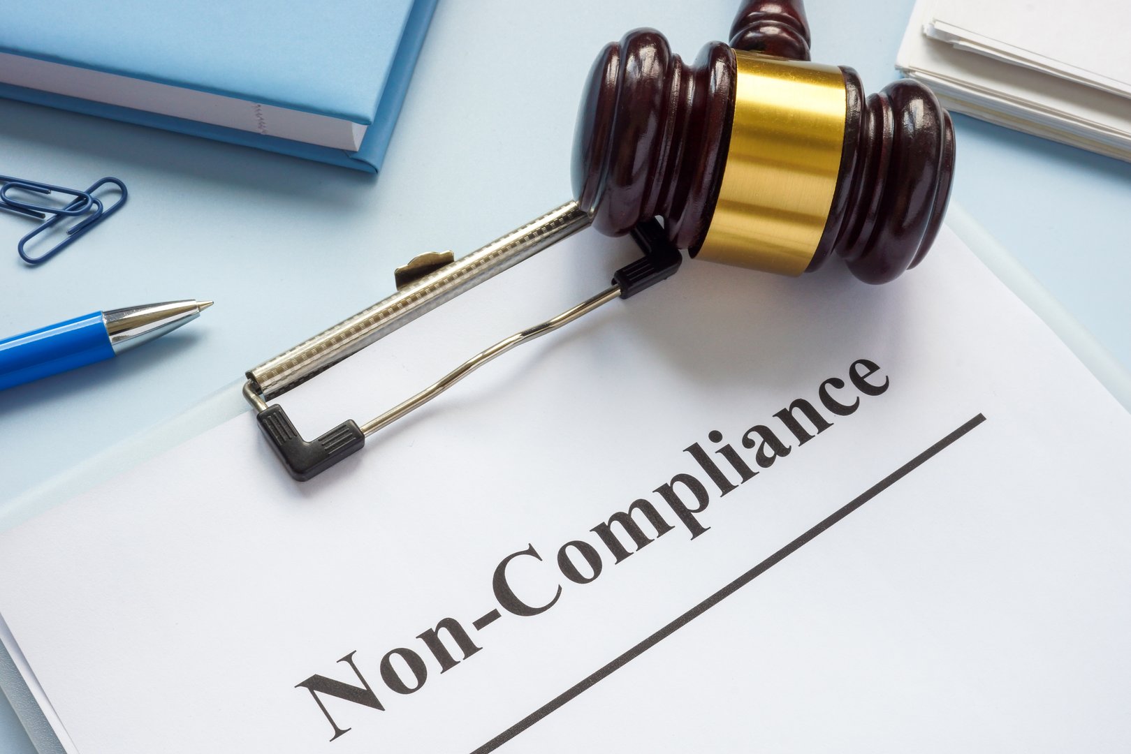 A clipboard with document about non-compliance and gavel.