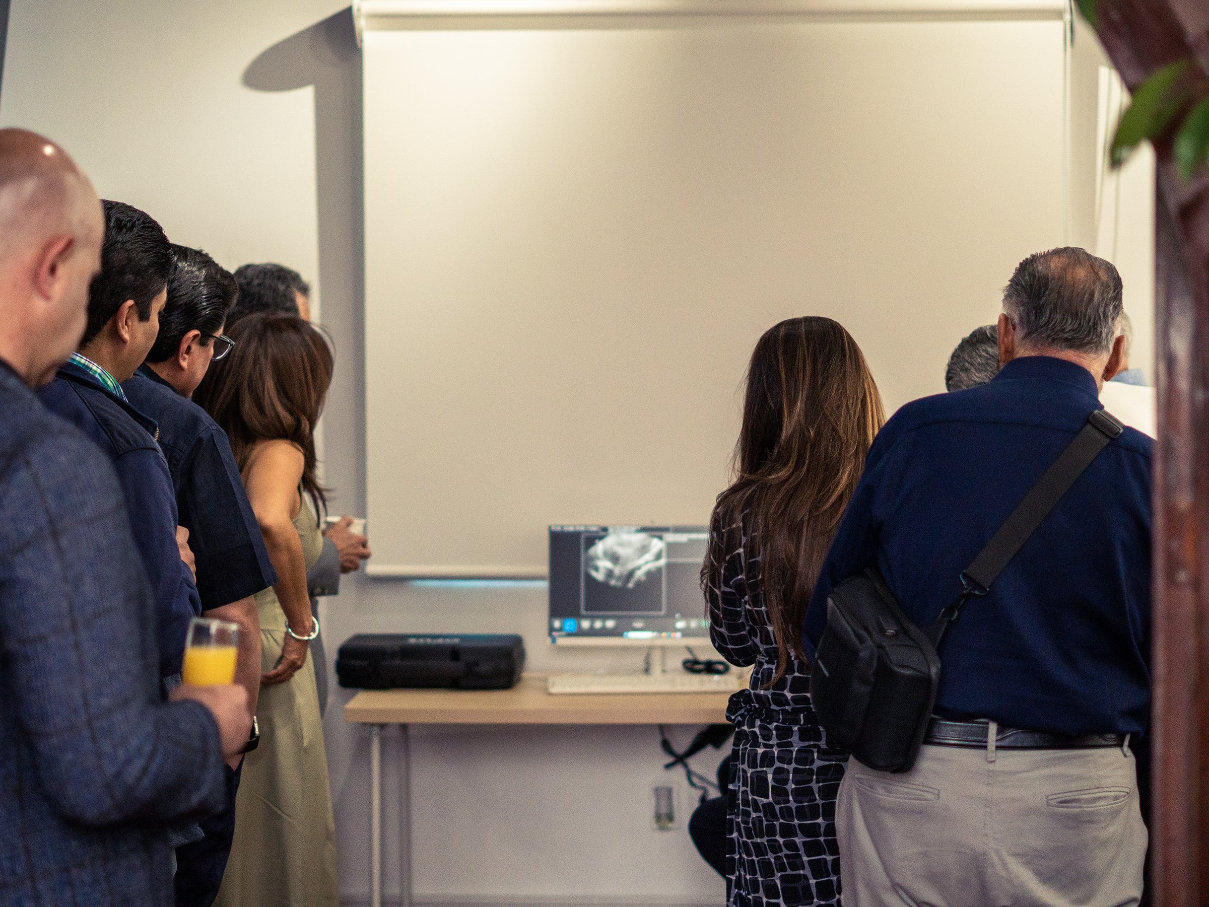 People gathered around a computer displaying an X-ray image in a room with minimal decor.