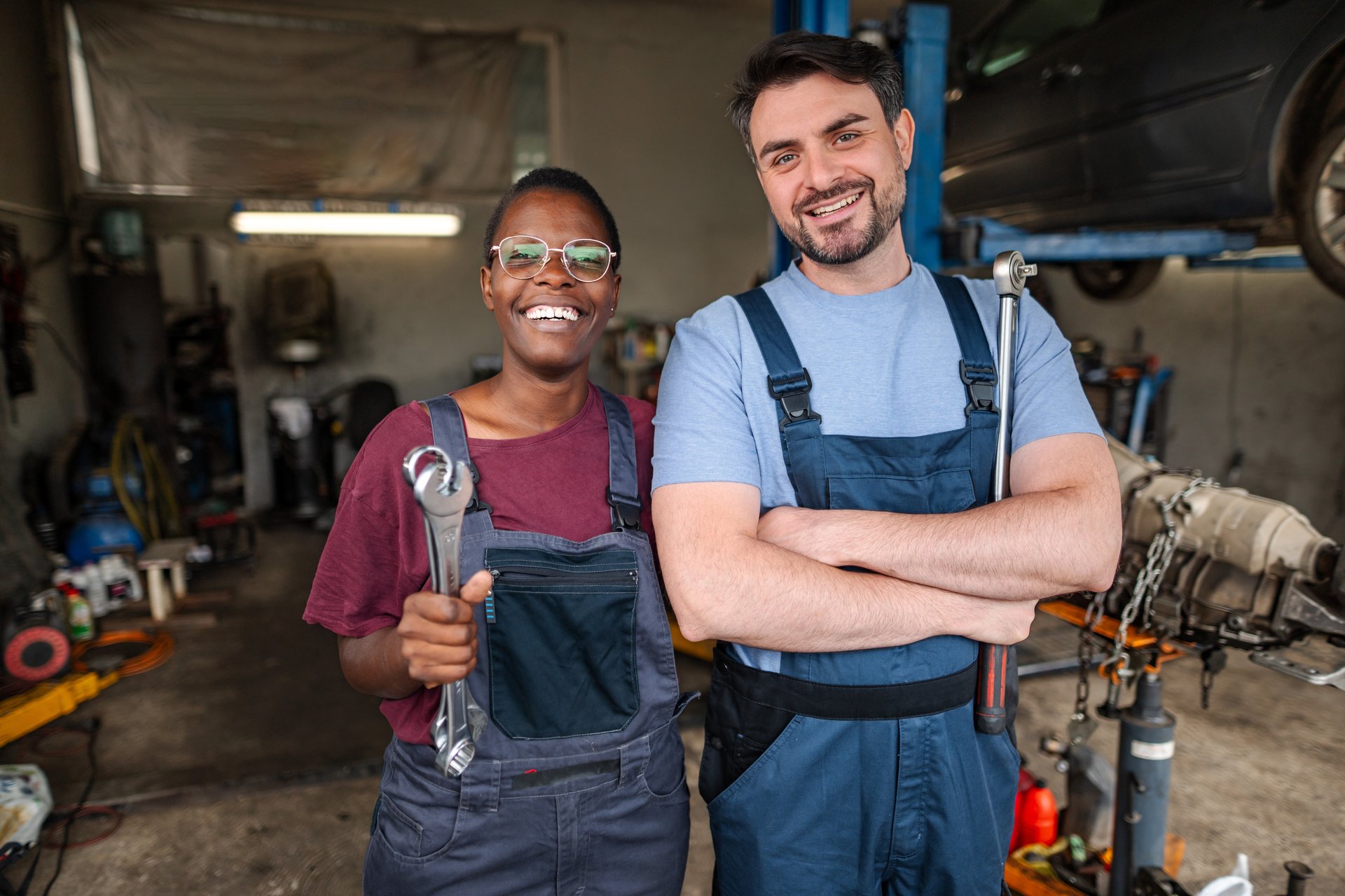 Two happy mechanics smiling and holding wrenches, standing in their auto repair shop