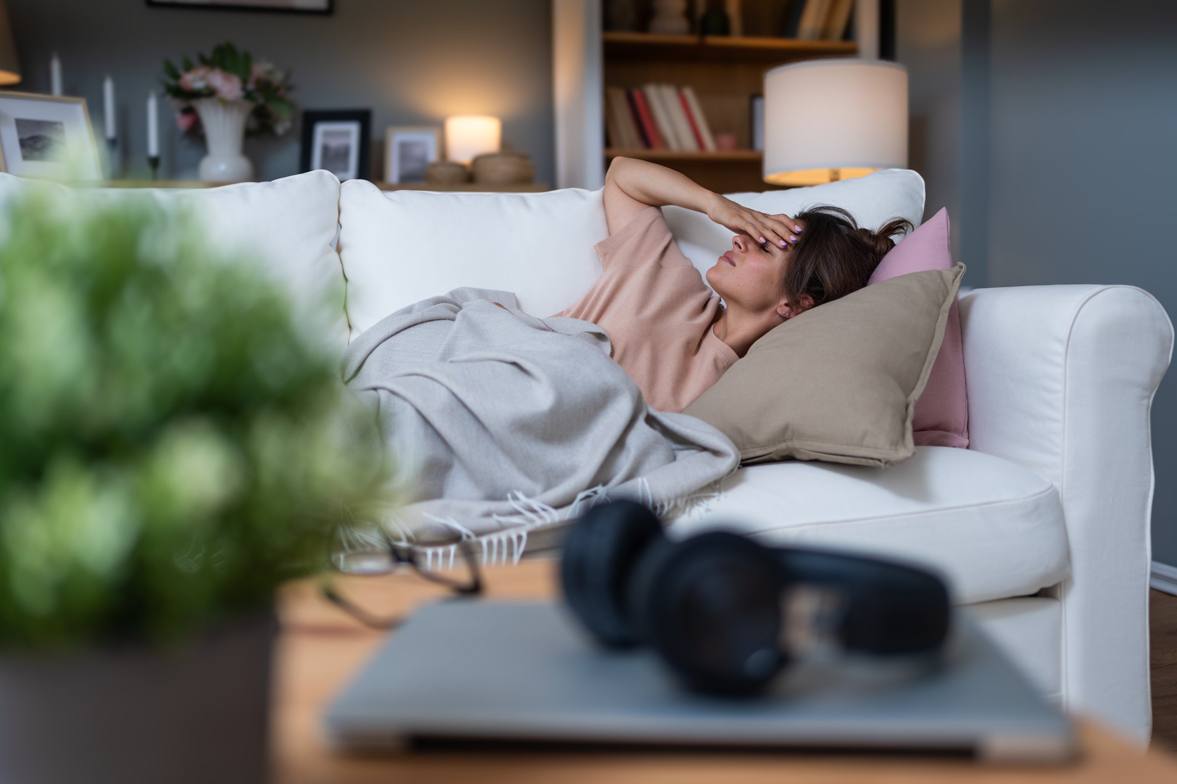 Woman sleeping on couch at home resting wrapping in plaid feeling bad symptoms. Girl suffering from seasonal flu or cold. Feel unhealthy with influenza. Tired exhausted workaholic becoming ill, sick.