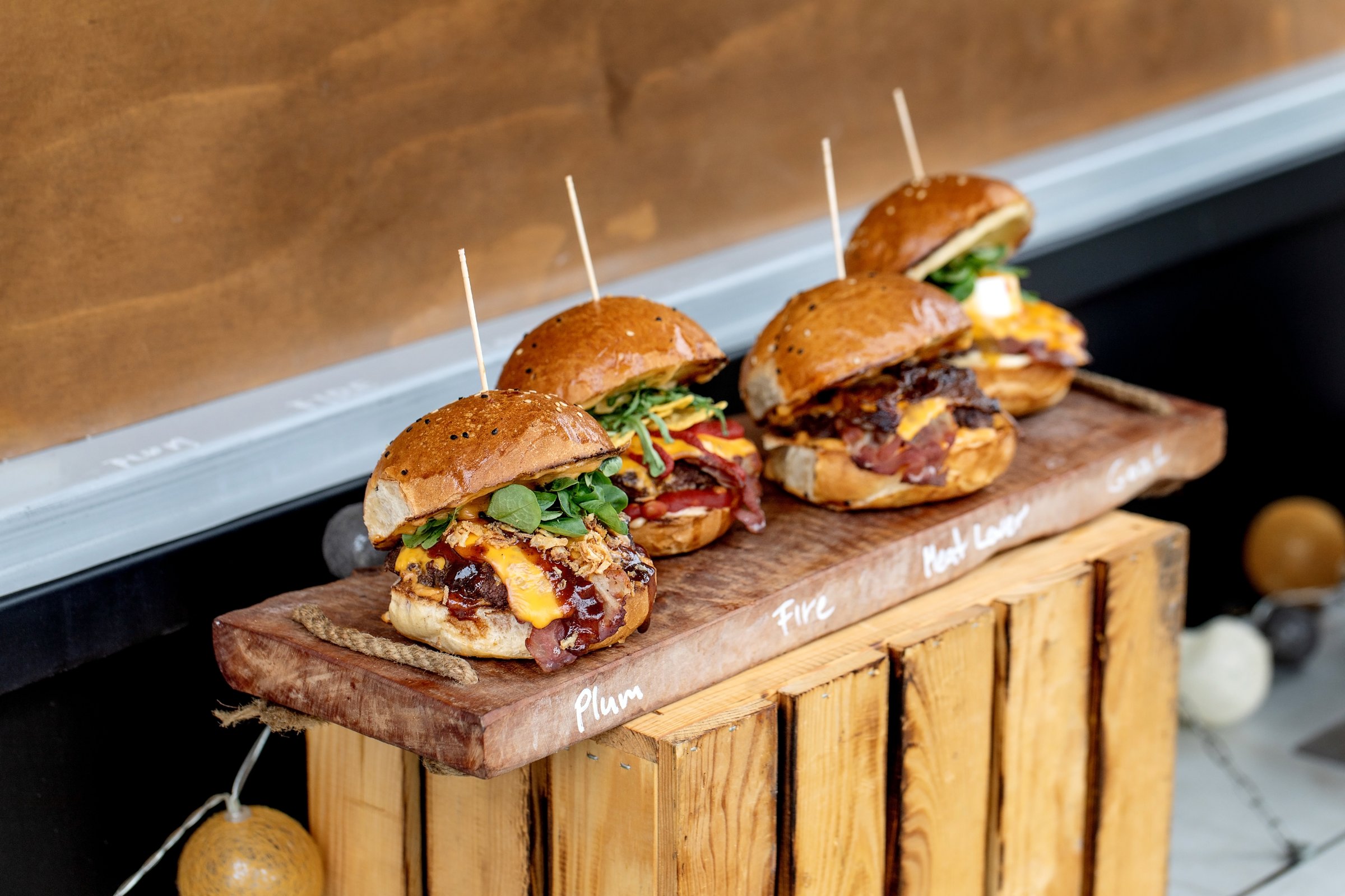 Mini burgers with melted cheese bacon fresh greens on brioche buns served on rustic wooden board. Perfect appetizers for party or restaurant menu.