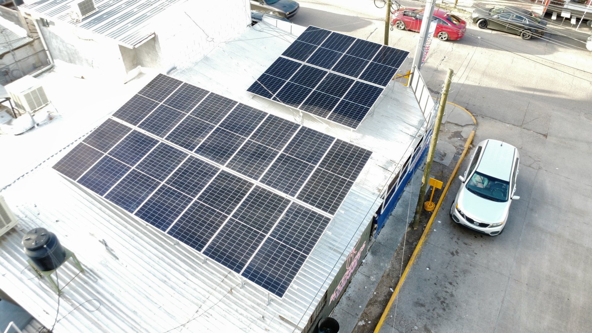 Rooftop with solar panels on a corrugated metal surface, a parked car nearby, and adjacent street in view.