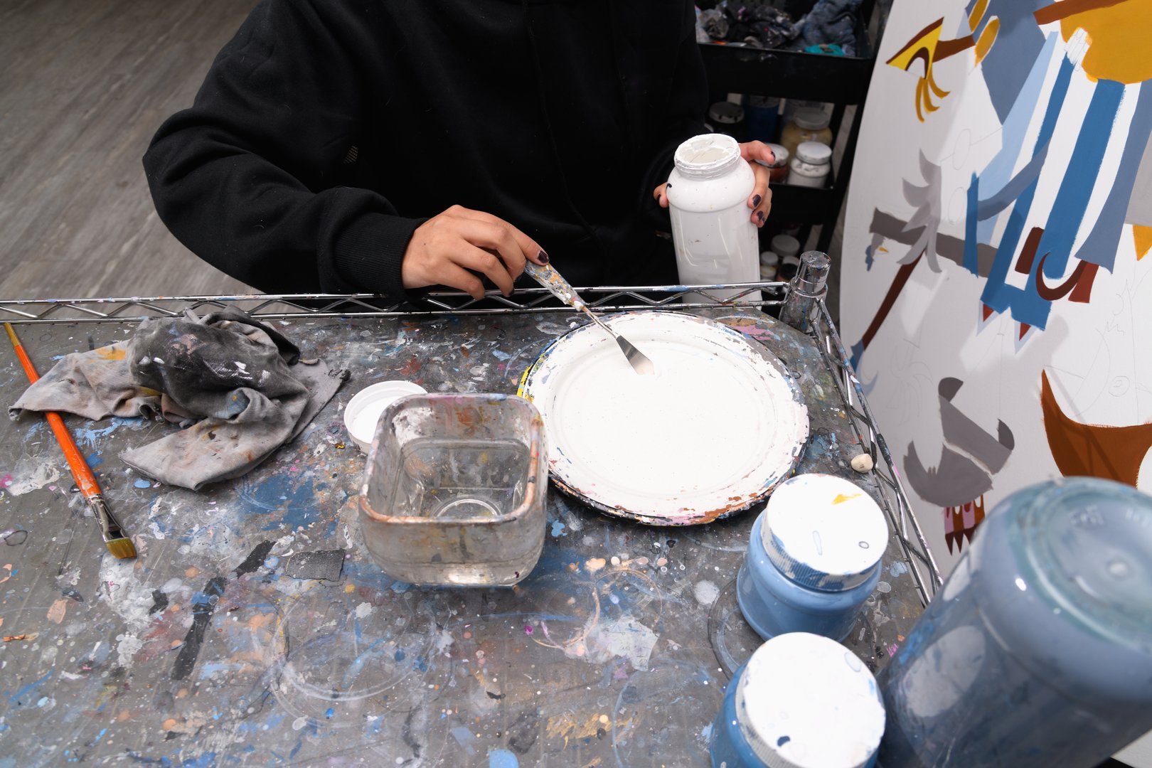 Manos de persona usando espátula para mezclar pintura blanca en plato