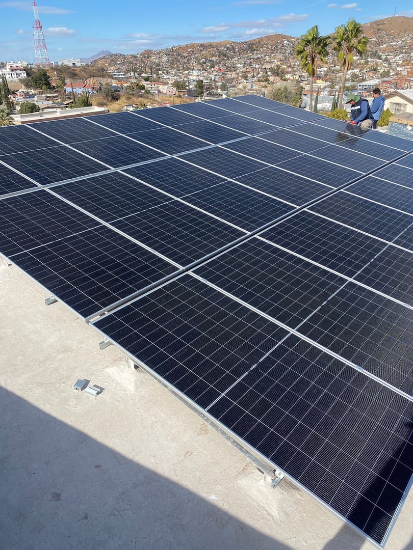 Solar panels installed on a rooftop with a cityscape and mountains in the background.