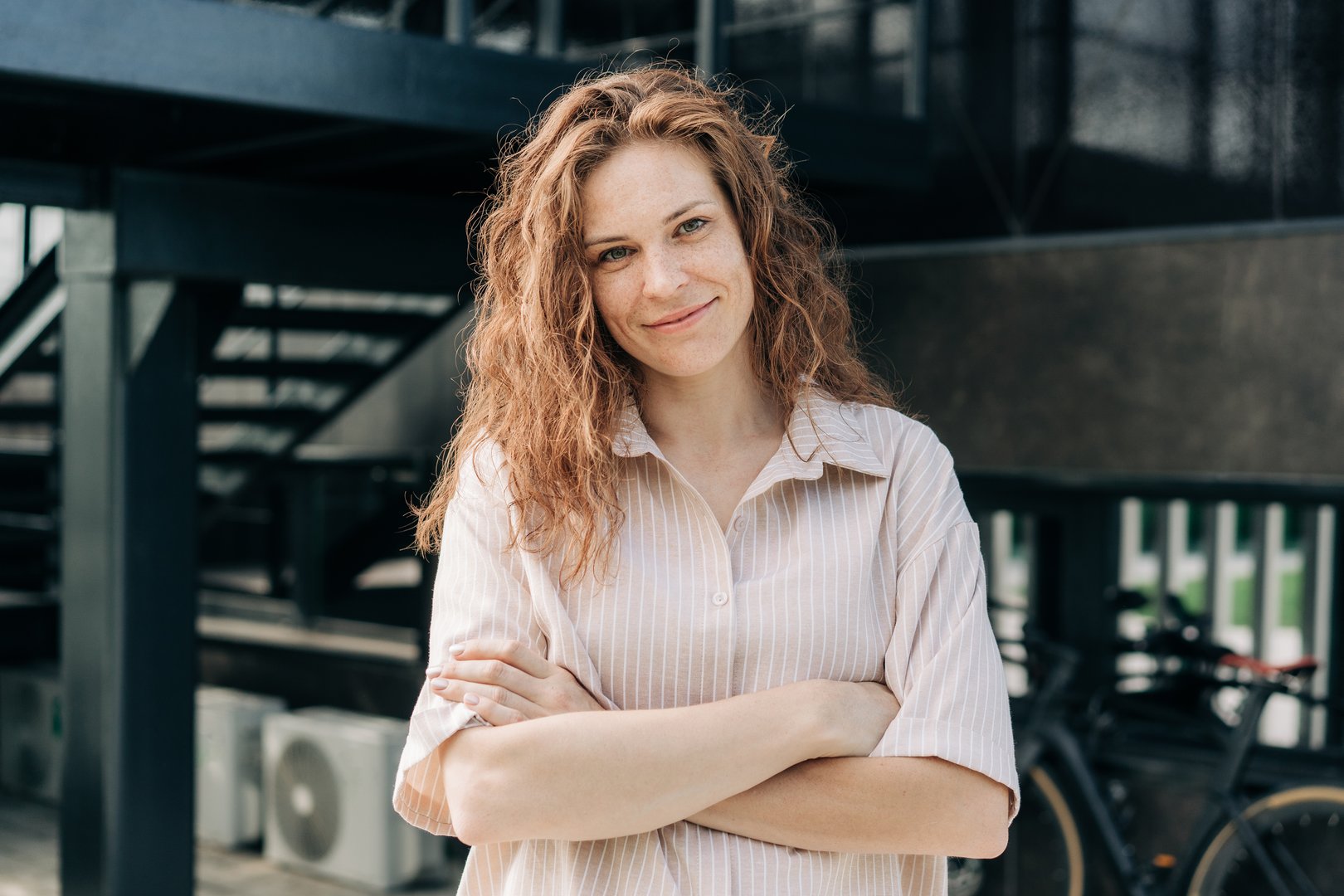A beautiful confident woman stands with her arms crossed against the background of a modern city building.