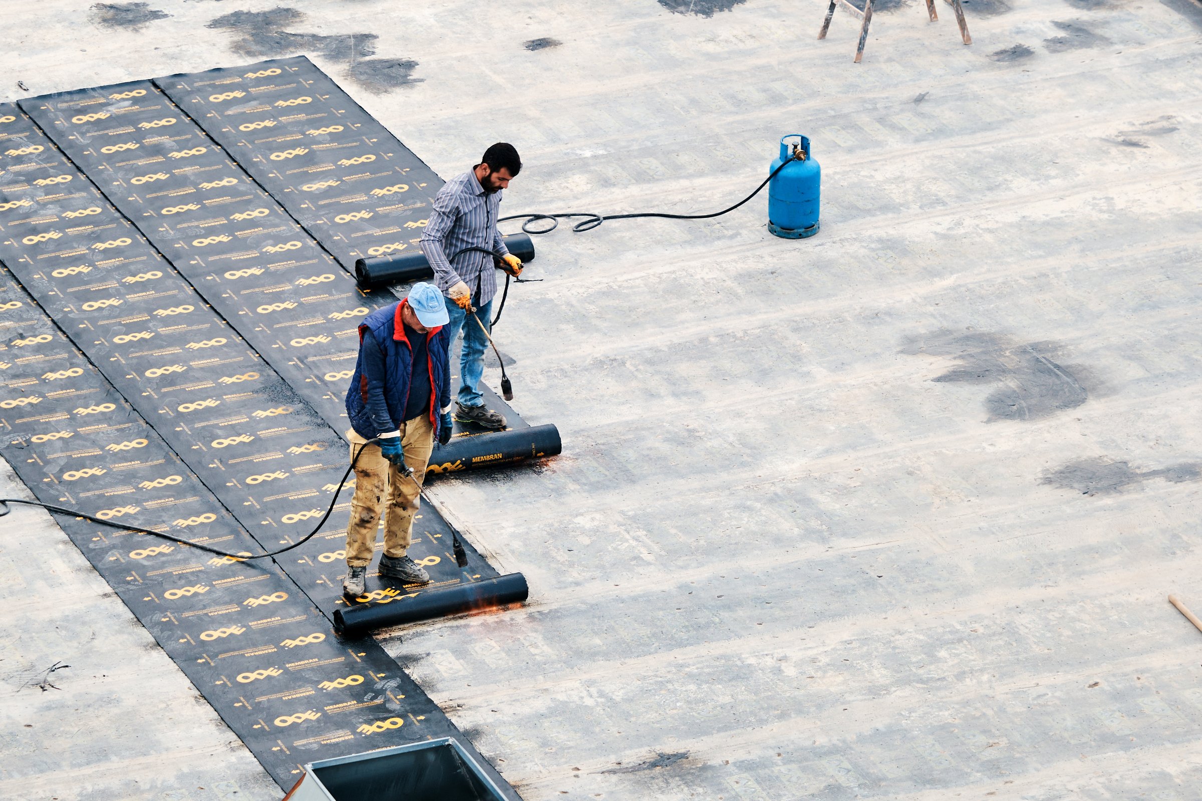 Ankara, Turkey - November 11, 2025: Construction workers using a torch to melt and apply a protective bituminous membrane for roof waterproofing and insulation.