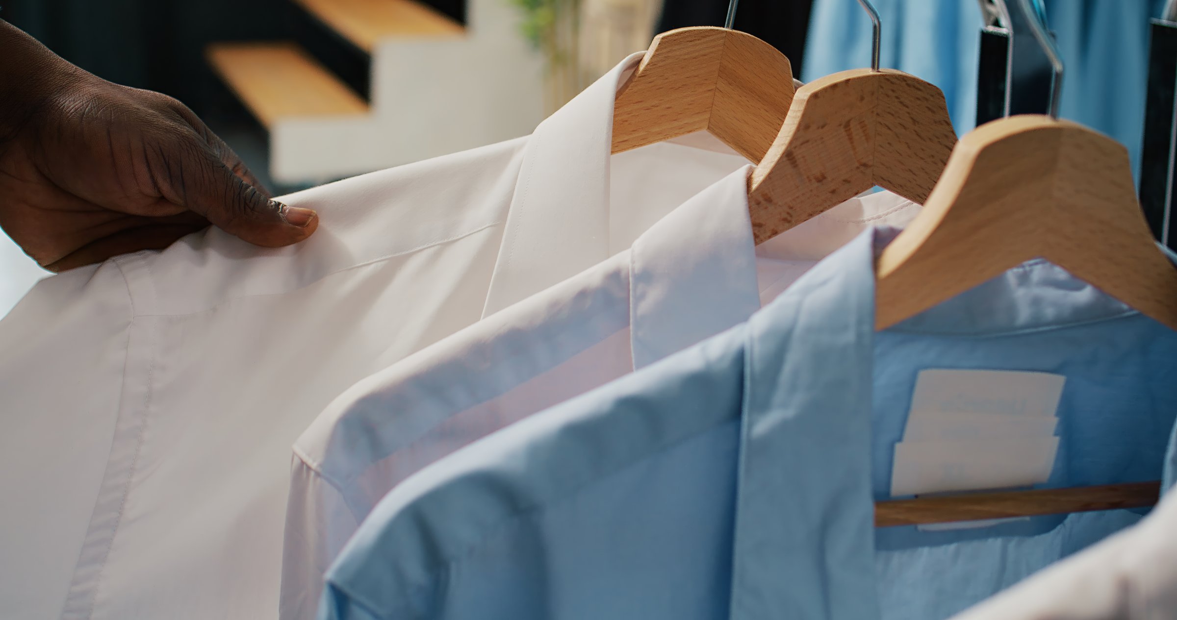 African american client looking at elegant classy shirts on hangers, shopping for formal wear to expand wardrobe. Customer searching for designer collection at department store. Close up. Camera B.