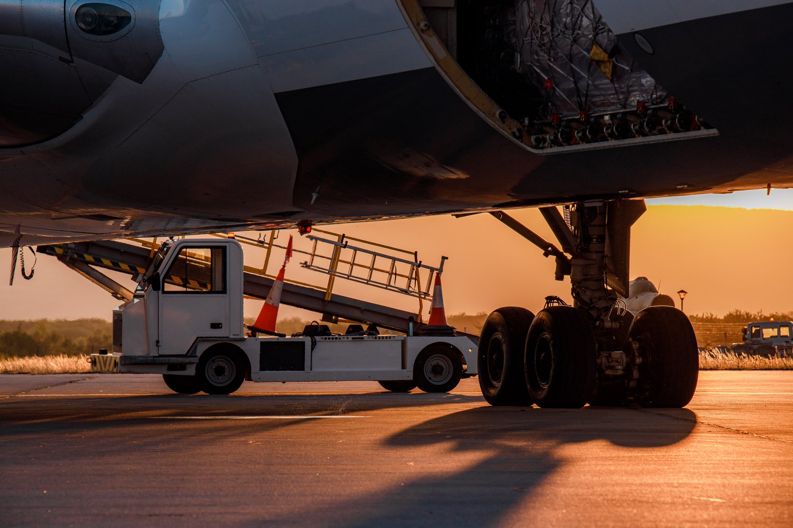 Ground support vehicle is positioned by an aircraft under a warm sunset glow at an airport.