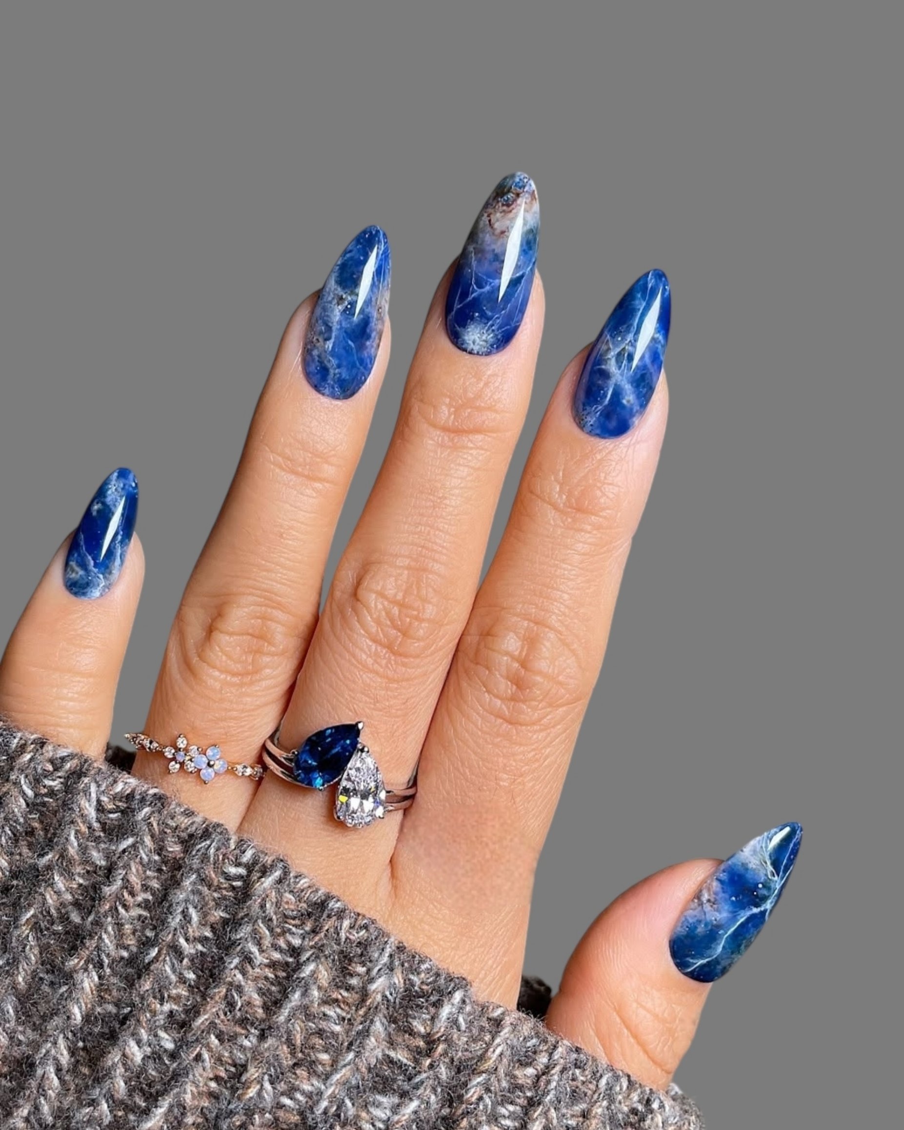 Hands and fingers of a young woman with modern innovative nail manicure with different and varied drawings with gold rings on her fingers with a gray background