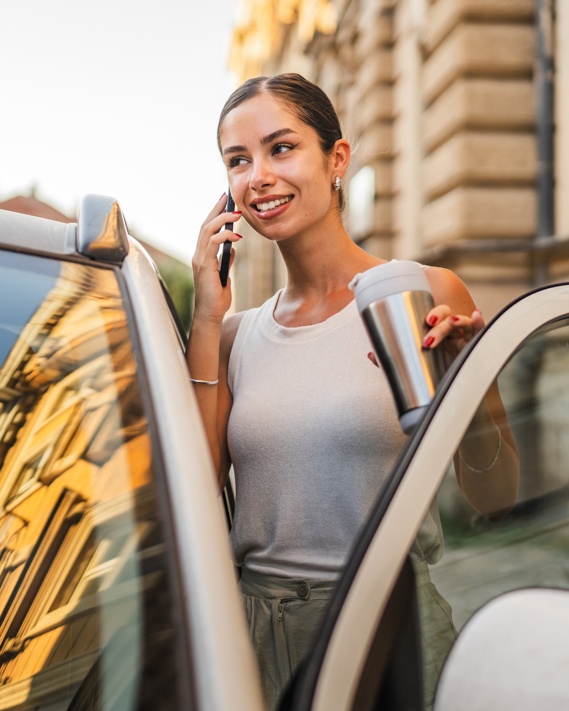 Young woman talk on mobile phone while get into her car on the street