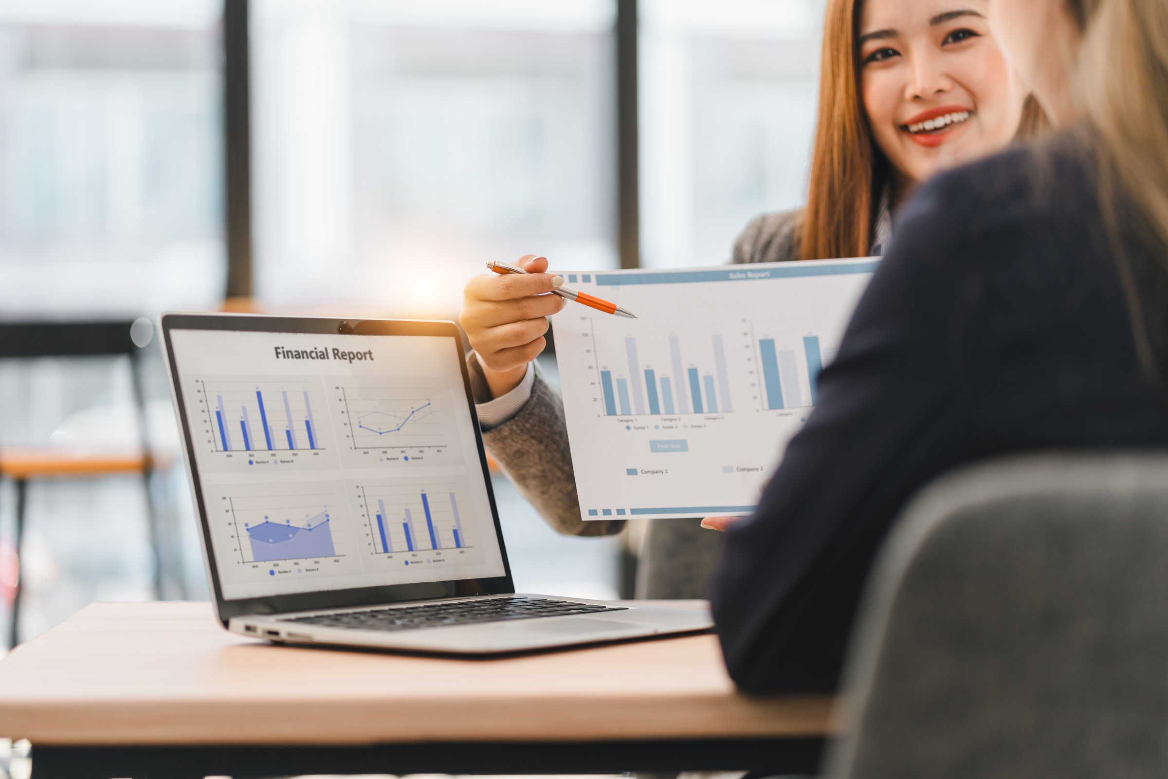 A Two business professionals discussing financial reports displayed on laptops in modern office setting, emphasizing teamwork and data analysis