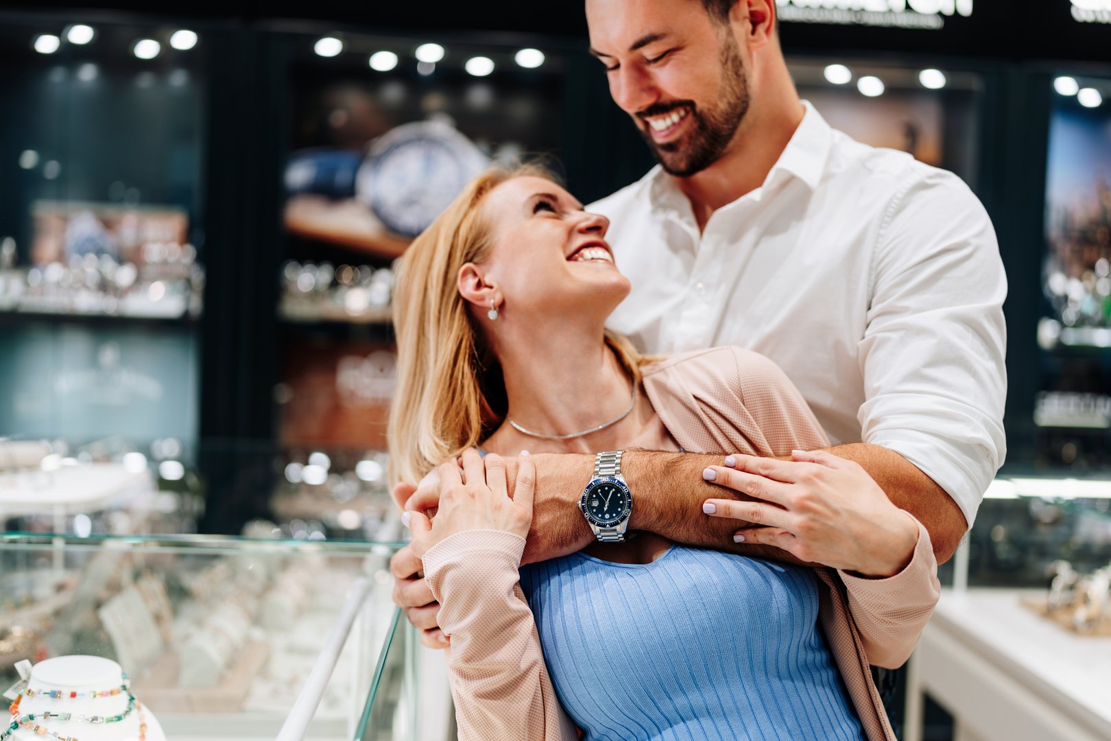 Young loving couple hugging and smiling while shopping for jewelry in a exclusive jewelry store, enjoying their time together and looking for the perfect piece