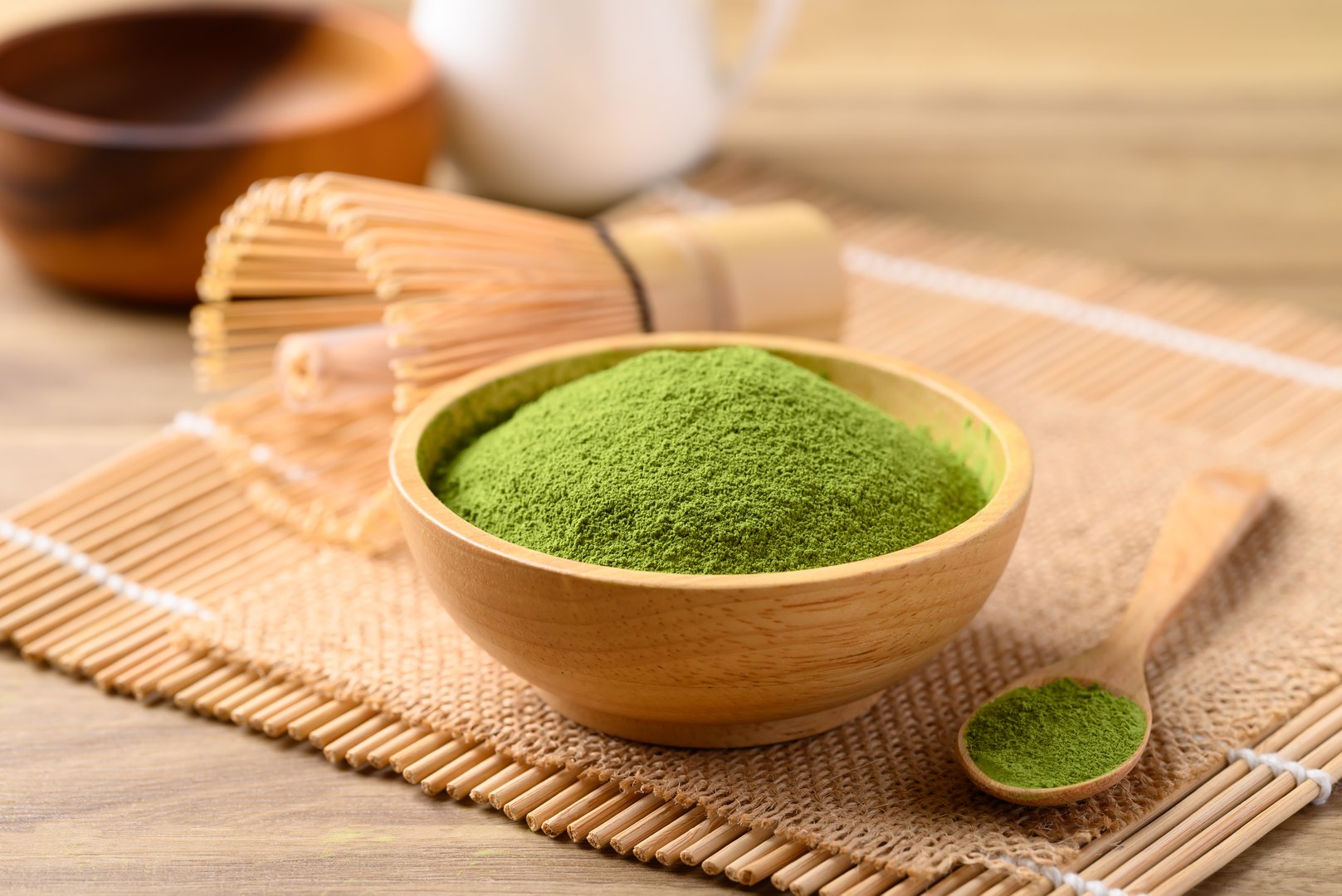 Matcha green tea powder in wooden bowl with spoon and chasen