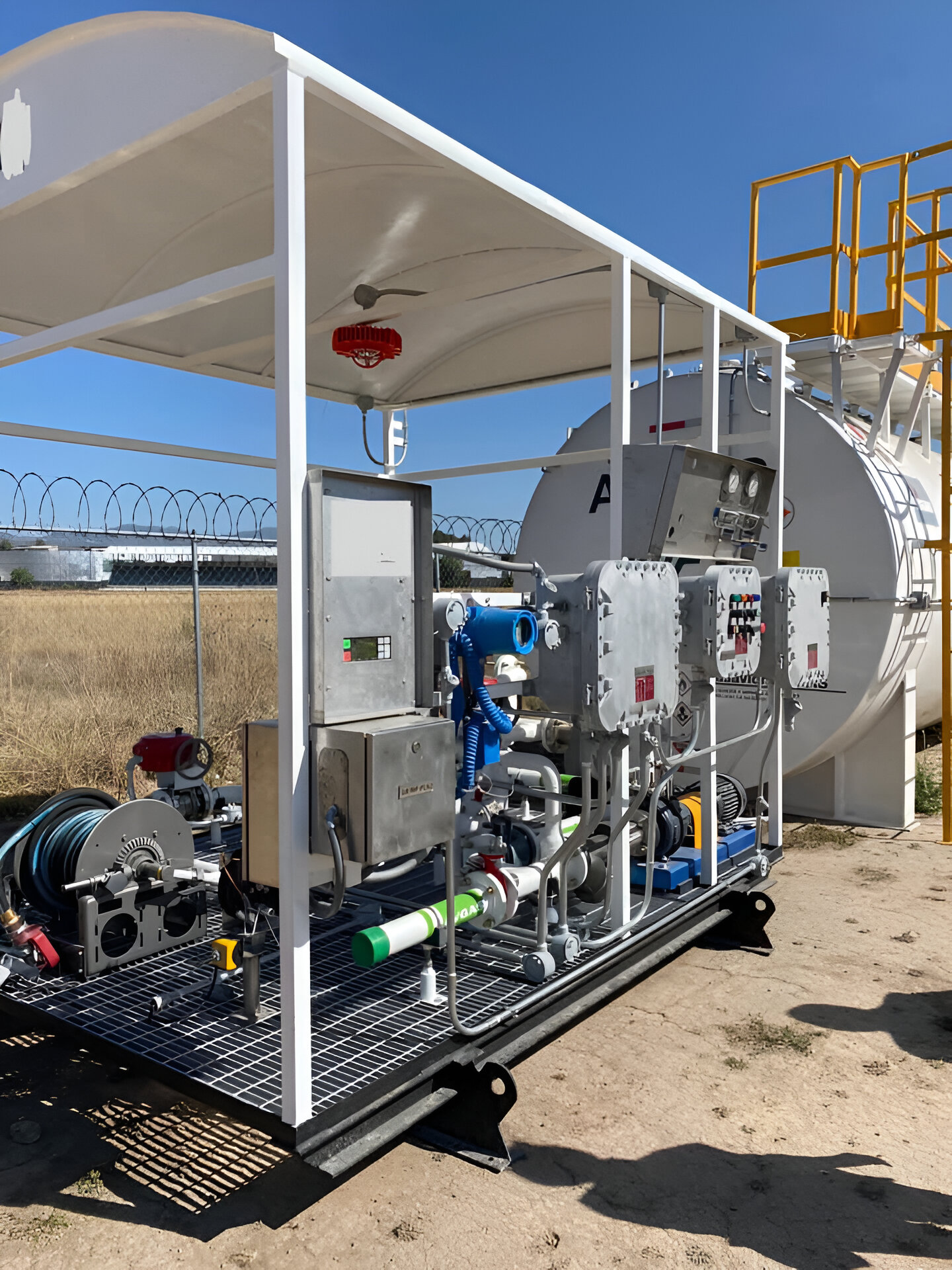 Industrial equipment setup with control panel, pipes, and hoses on a metal platform, located outdoors near fencing.