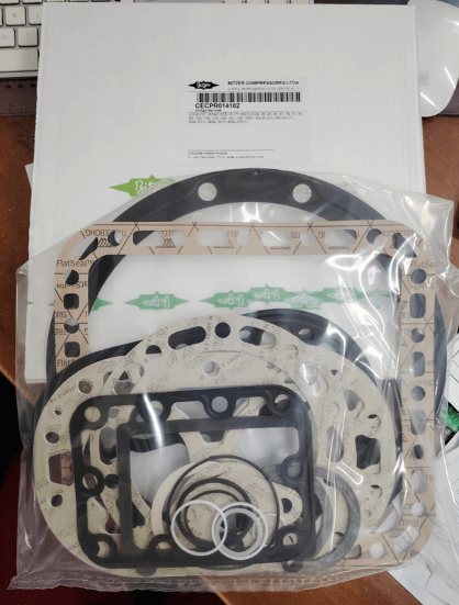 A set of engine gaskets and seals in a plastic bag, placed on a white package, ready for shipping or assembly.