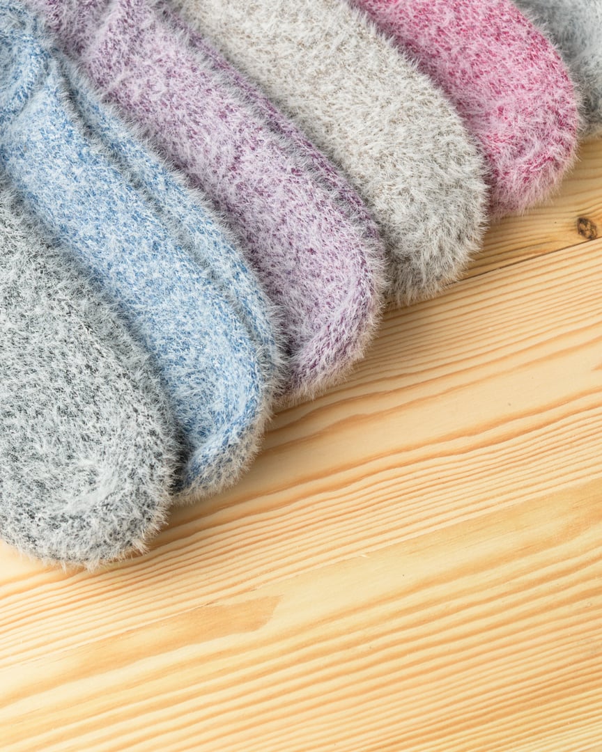 Fluffy pastel socks arranged on wooden background with ample copy space radiate warmth, comfort, and cozy home atmosphere for versatile design.