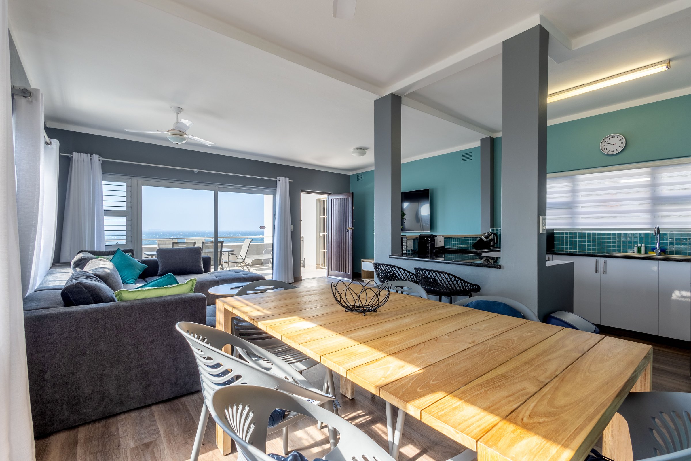 Bright living space with a large dining table, modern kitchen, and ocean view from the balcony.