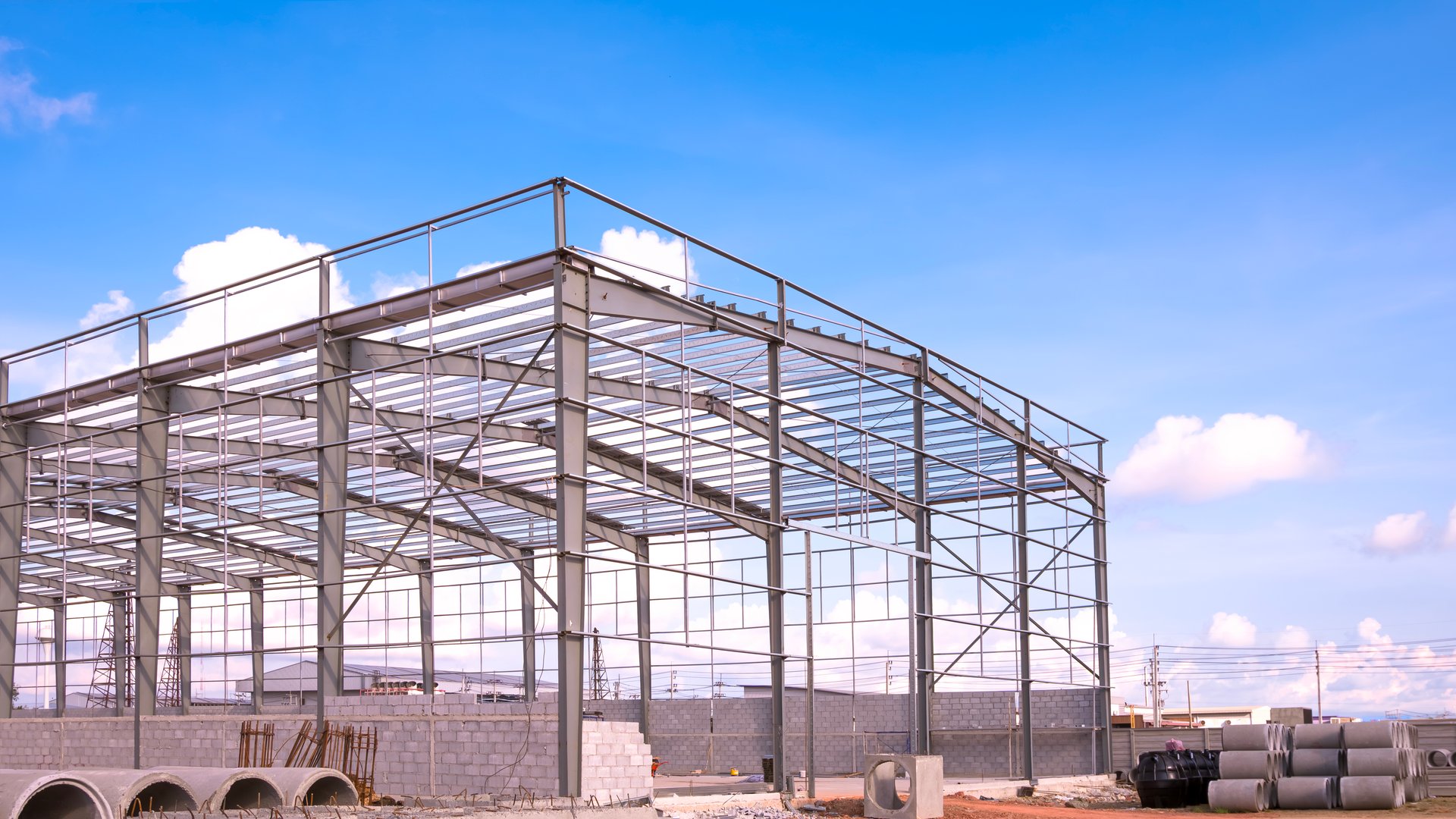 Metal column and roof beam structure of industry warehouse factory building with material in construction site against blue sky background, side view with copy space