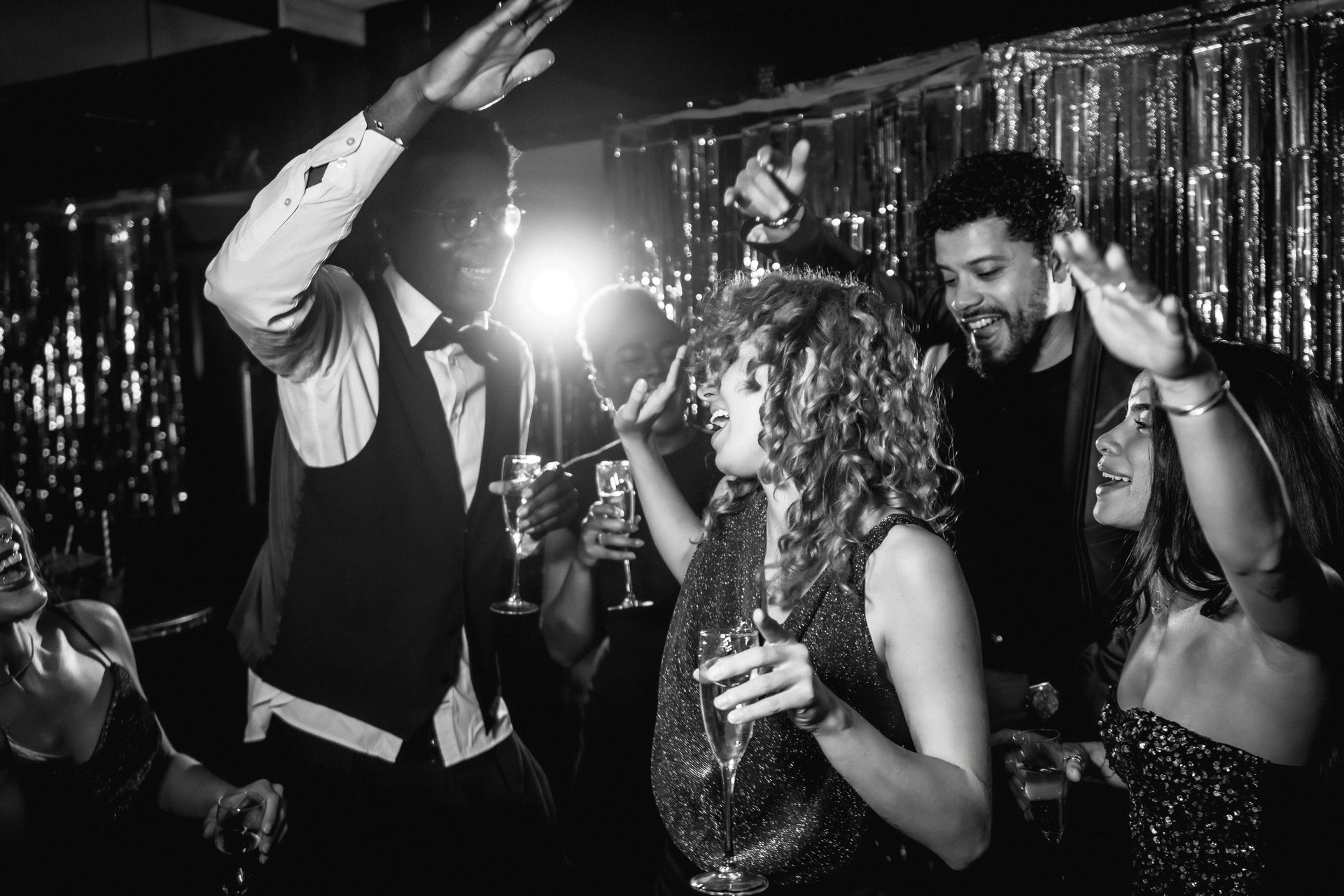 Group of stylish friends dancing joyfully and sipping champagne at a lively nightclub party, celebrating together in a vibrant atmosphere