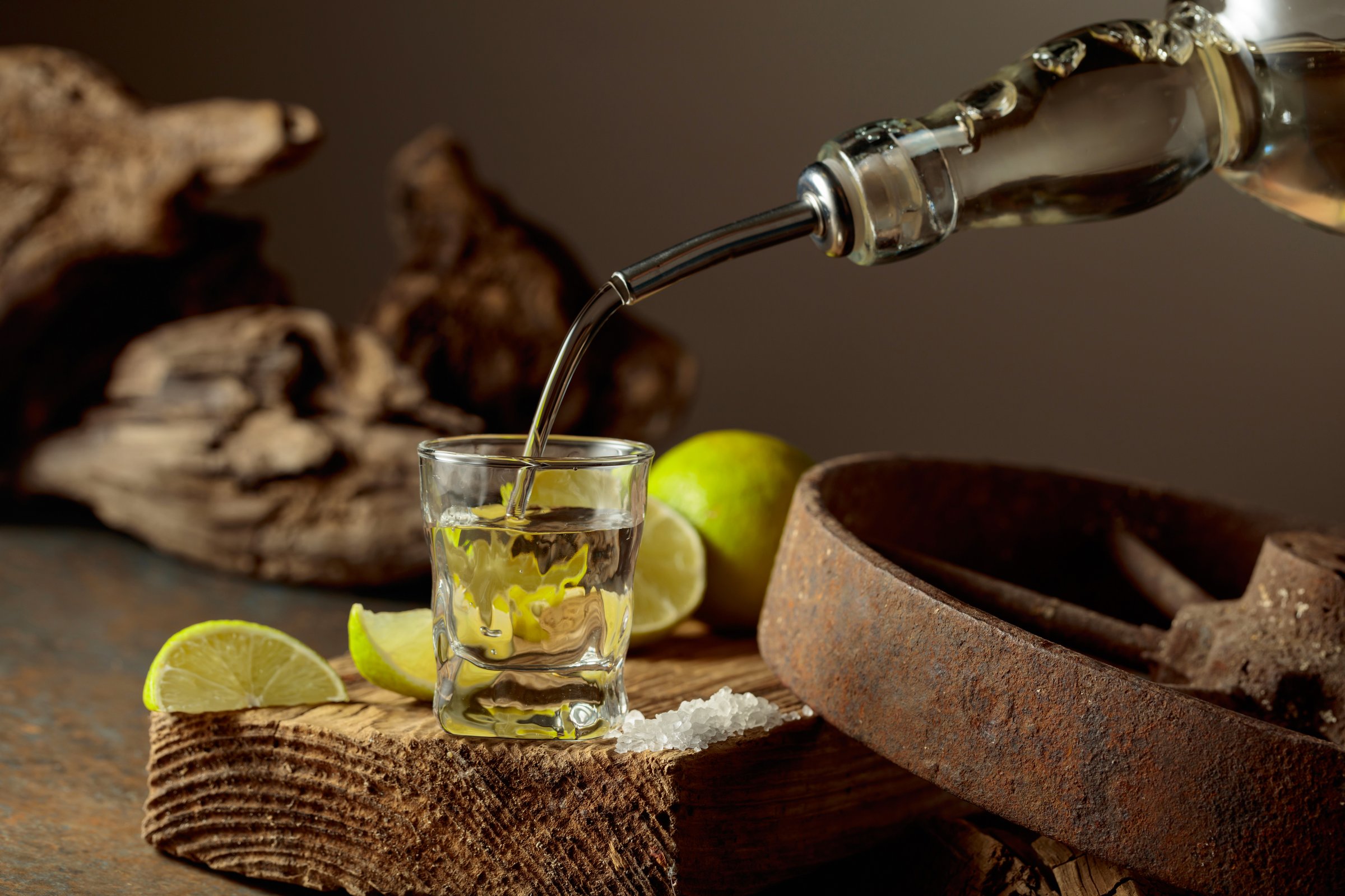 Tequila with salt and lime slices on a wooden board. Tequila is poured from a bottle into a glass. Vintage background with old wood and rusty metal.