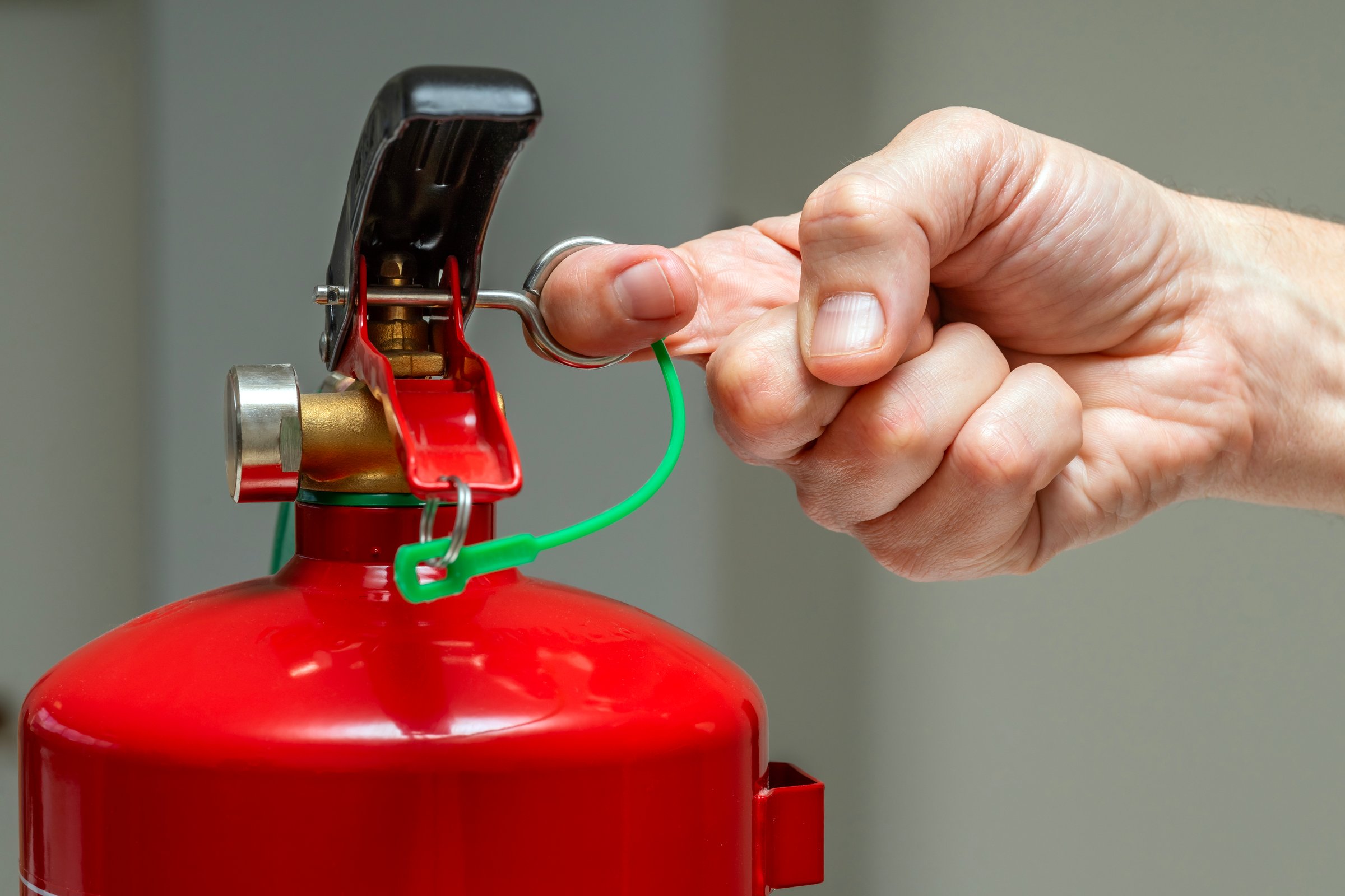 Close up of a male hand pulling a manual chemical fire extinguisher safety pin. Fire drill training and teaching.