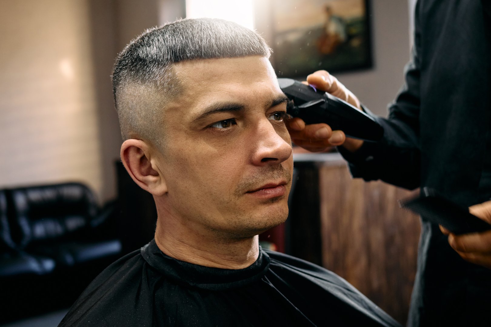 A skilled hairdresser is giving a man a fresh haircut in a contemporary barbershop. The atmosphere is relaxed, with natural light illuminating the space.