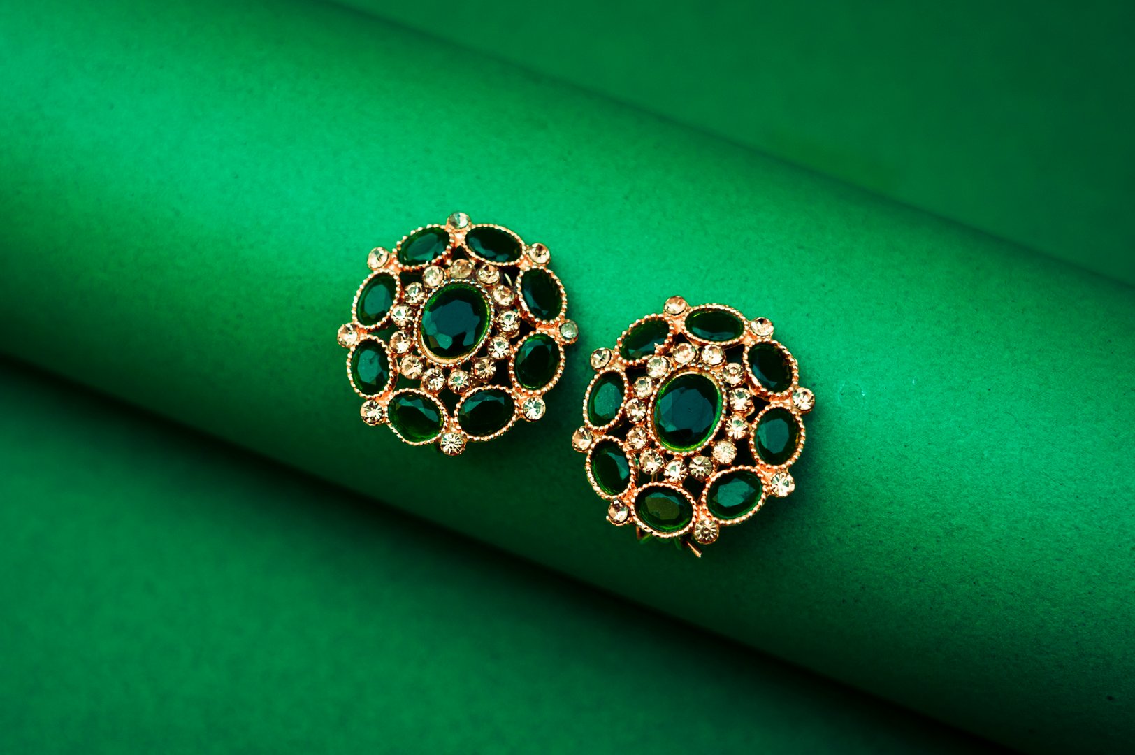 Elegant Gold Earrings With Green Genstones on Fresh Green Backdrop, Close-up of gold-plated earrings placed on a vibrant green background, highlighting luxury and natural elegance.