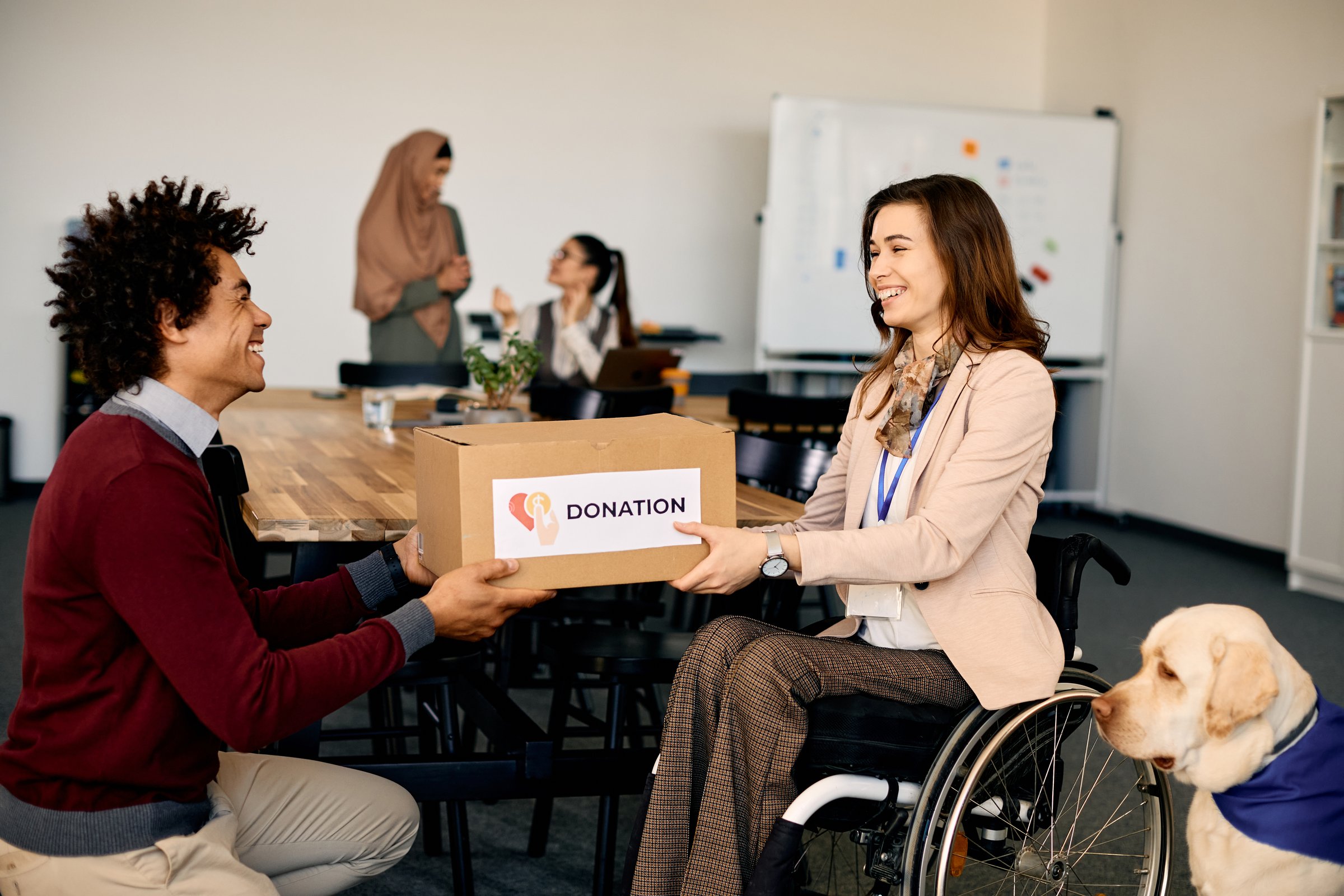 Happy businesswoman in wheelchair receiving donation box while working at charitable foundation.