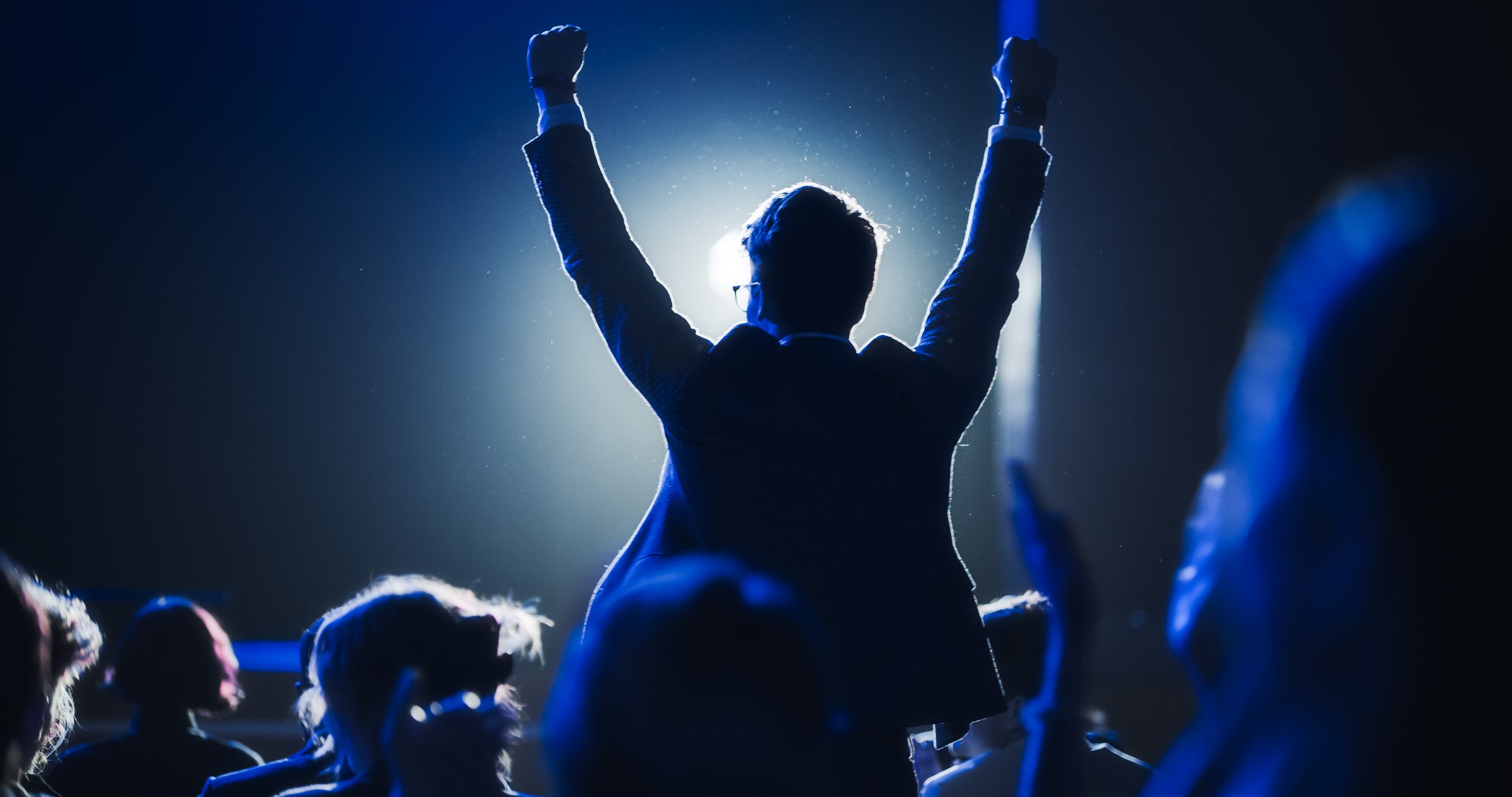 Young Excited Man Ecstatic About Winning the Coveted Business Person of the Year Award. Man Jumping After Winning the Event Category. Handsome Specialist Celebrating and Cheering a Colleague on Stage.