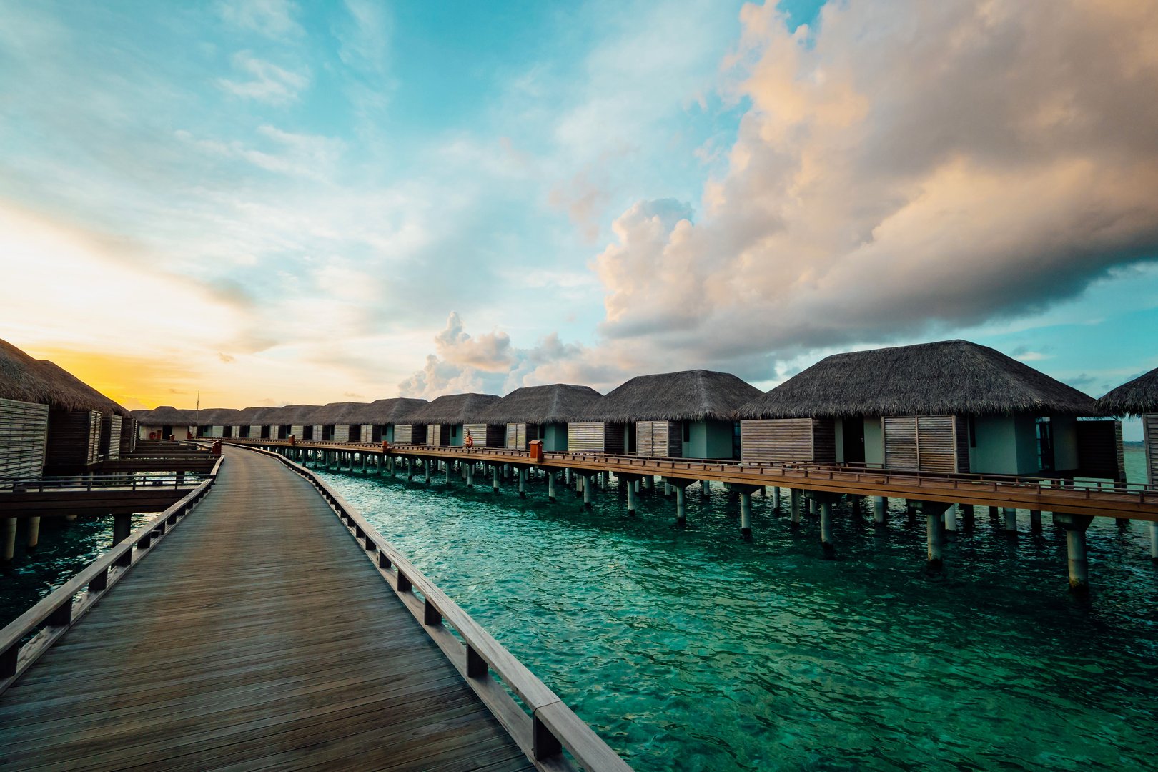 Scenic view of overwater bungalows in the Maldives at sunset with clear turquoise water and a vibrant sky.