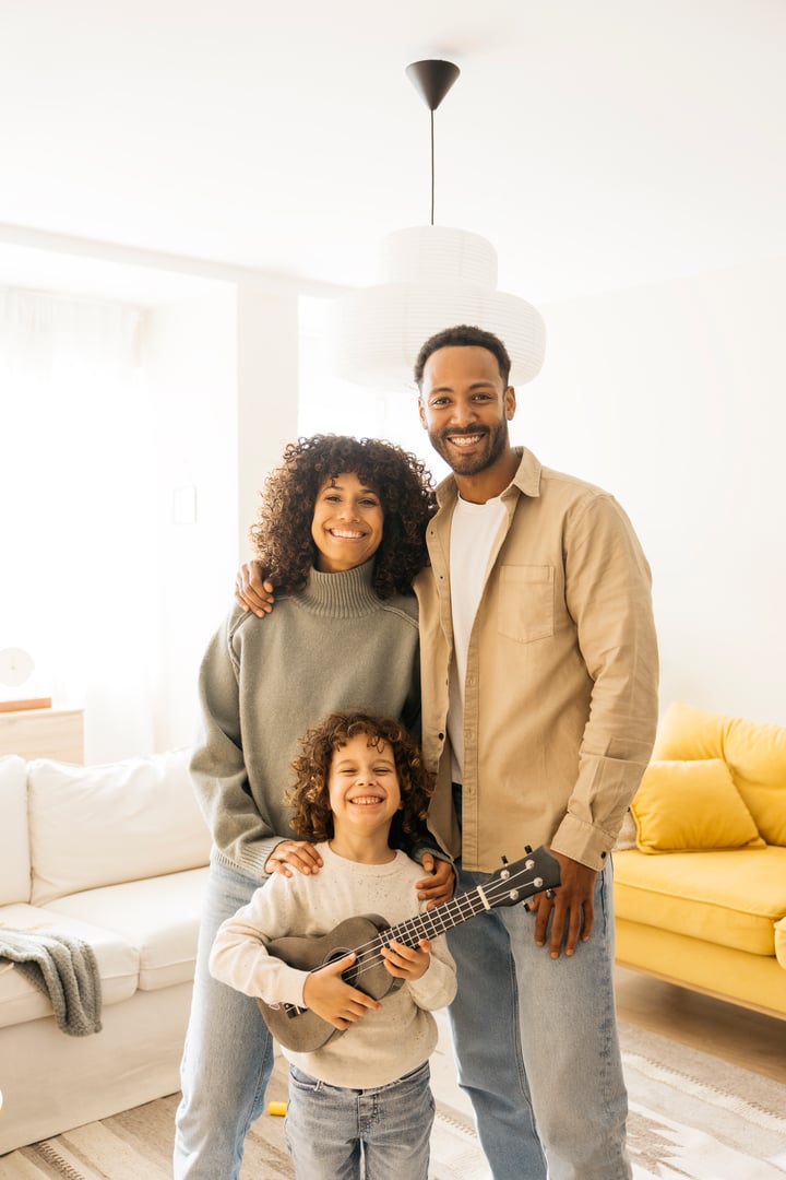 A cheerful family posing in a cozy home interior, with joyful expressions, featuring a young child holding a ukulele and parents embracing lovingly.