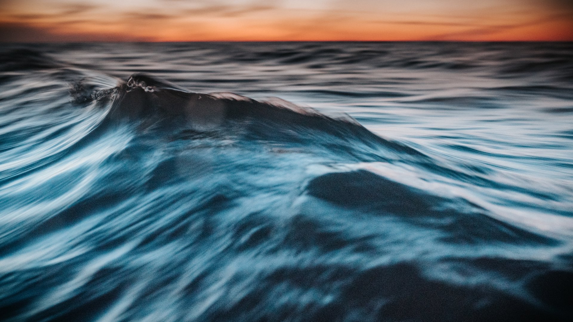 A close-up, artistic photograph capturing the gentle ripples of ocean water under soft evening light. The shallow depth of field adds a dreamy, abstract quality, emphasizing the texture and movement of the surface. Perfect for themes of tranquility, nature, meditation, and the power of water.
