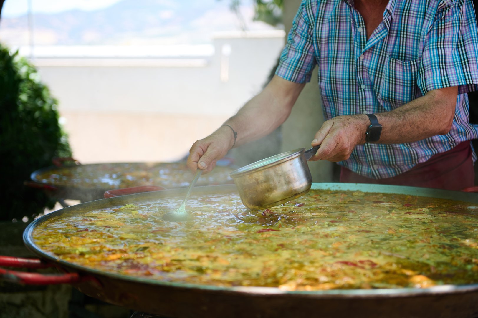 A chef skillfully prepares a large paella outdoors during a festive gathering in a picturesque Spanish village. This captures a moment of culinary tradition and celebration.