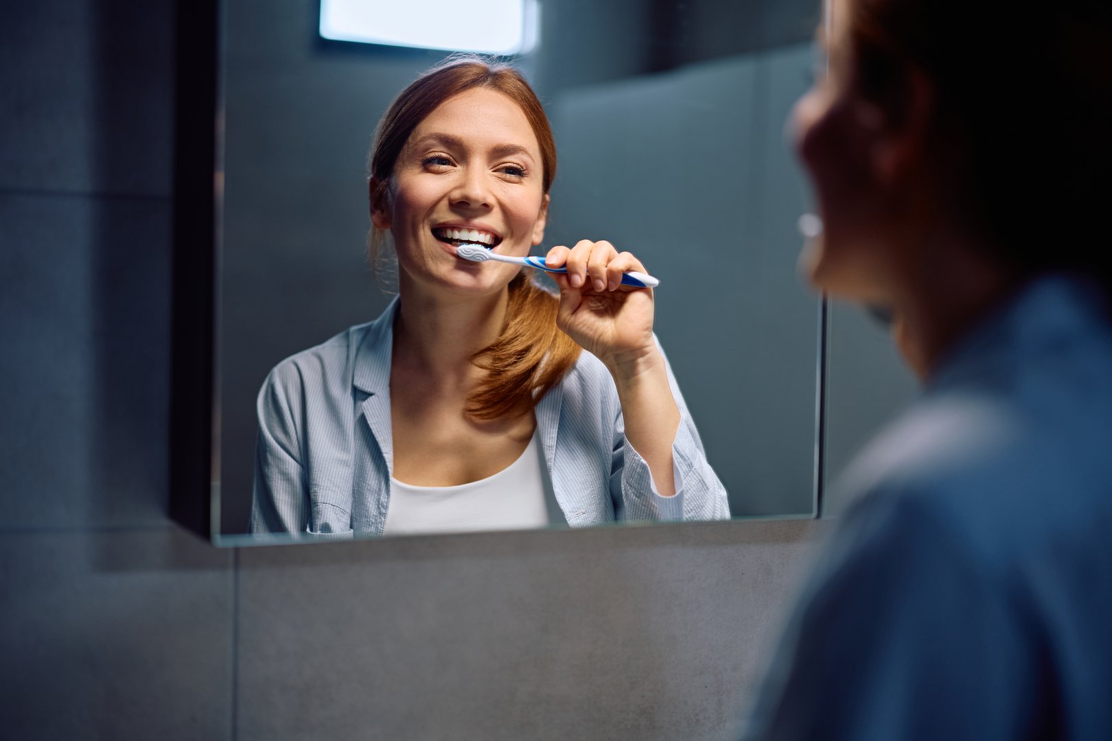 Reflection in a mirror of happy woman brushing teeth in the bathroom.