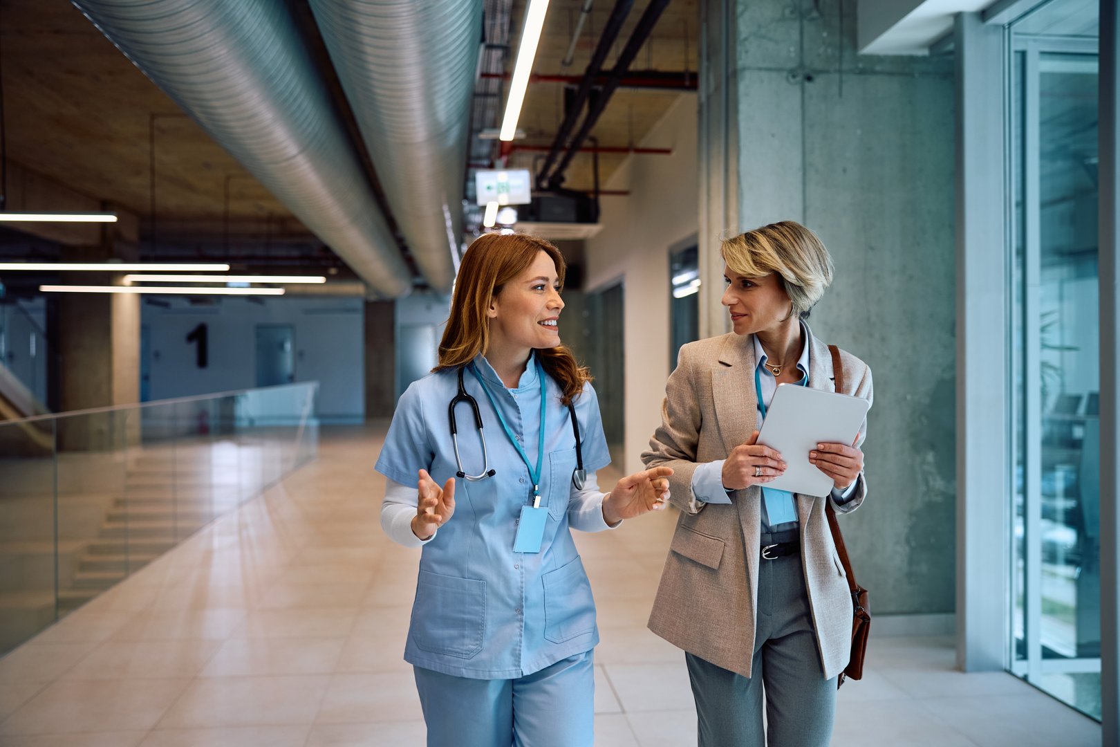 Happy female administrator communicating with a nurse while walking through medical clinic. Copy space.