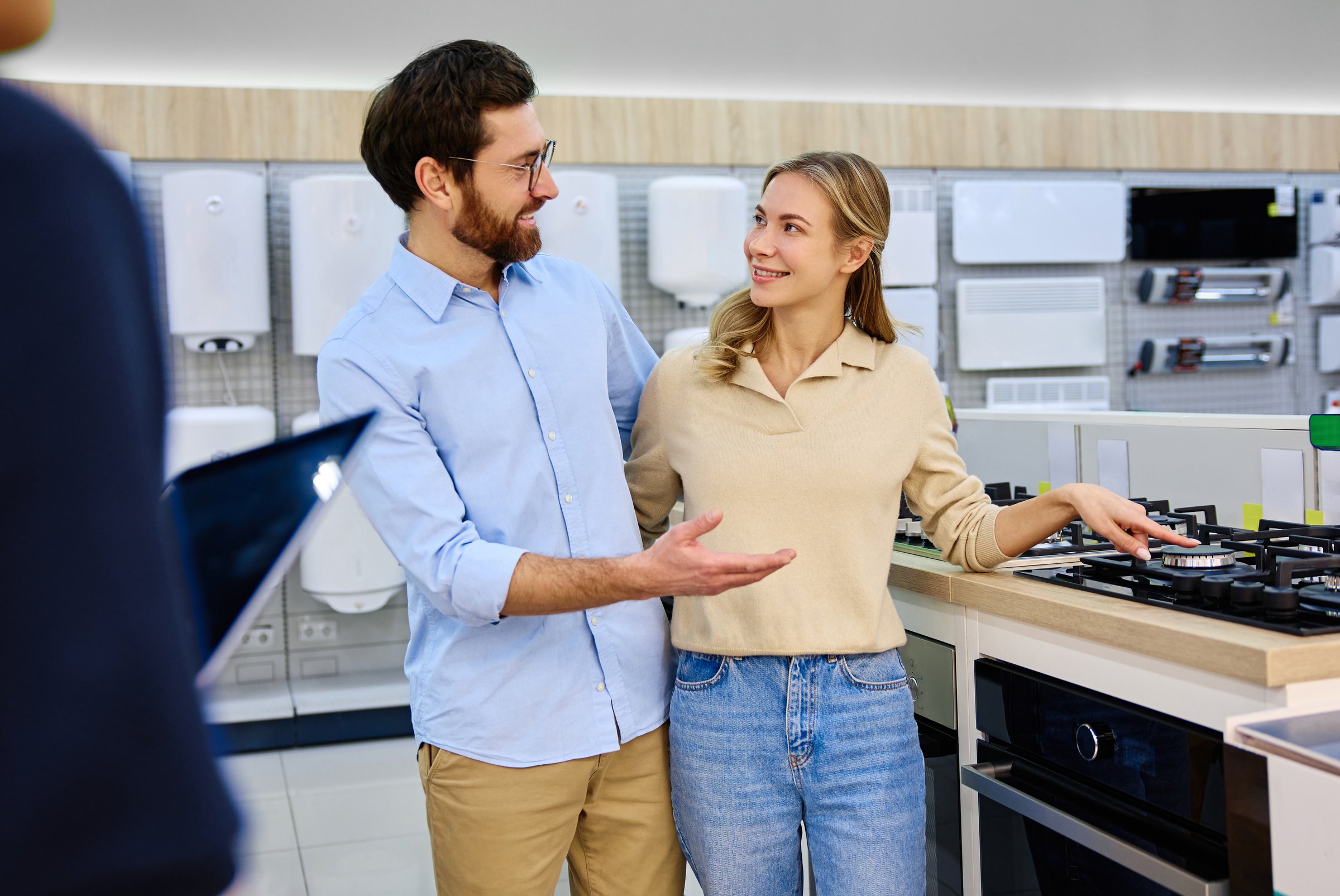 A young couple communicates and interacts in a bright and contemporary kitchen appliance showroom, where they are discussing various options and choices for their future new home together